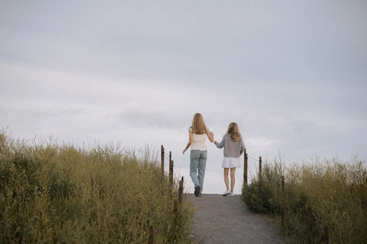 Perhekuvaus Helsinki, sisarukset kävelevät käsikkäin hiekkatiellä.