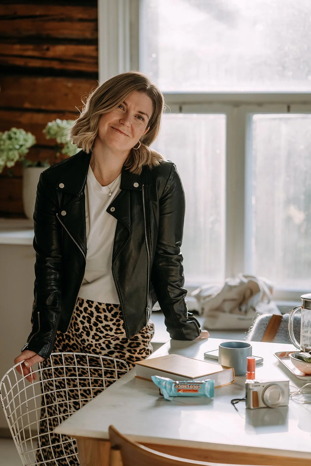 Yrittäjä ja valokuvaaja Heidi Väisänen seisoo ikkunan edessä ja hymyilee kameralle