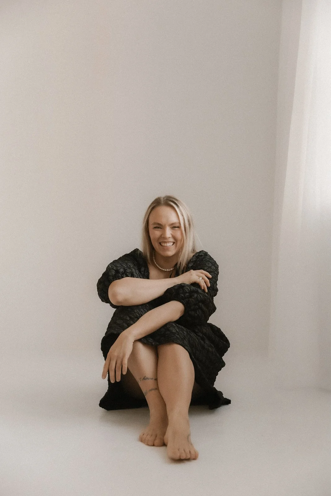 Yrityskuvaus studiossa. Yrittäjä istuu hymyillen studion lattialla.