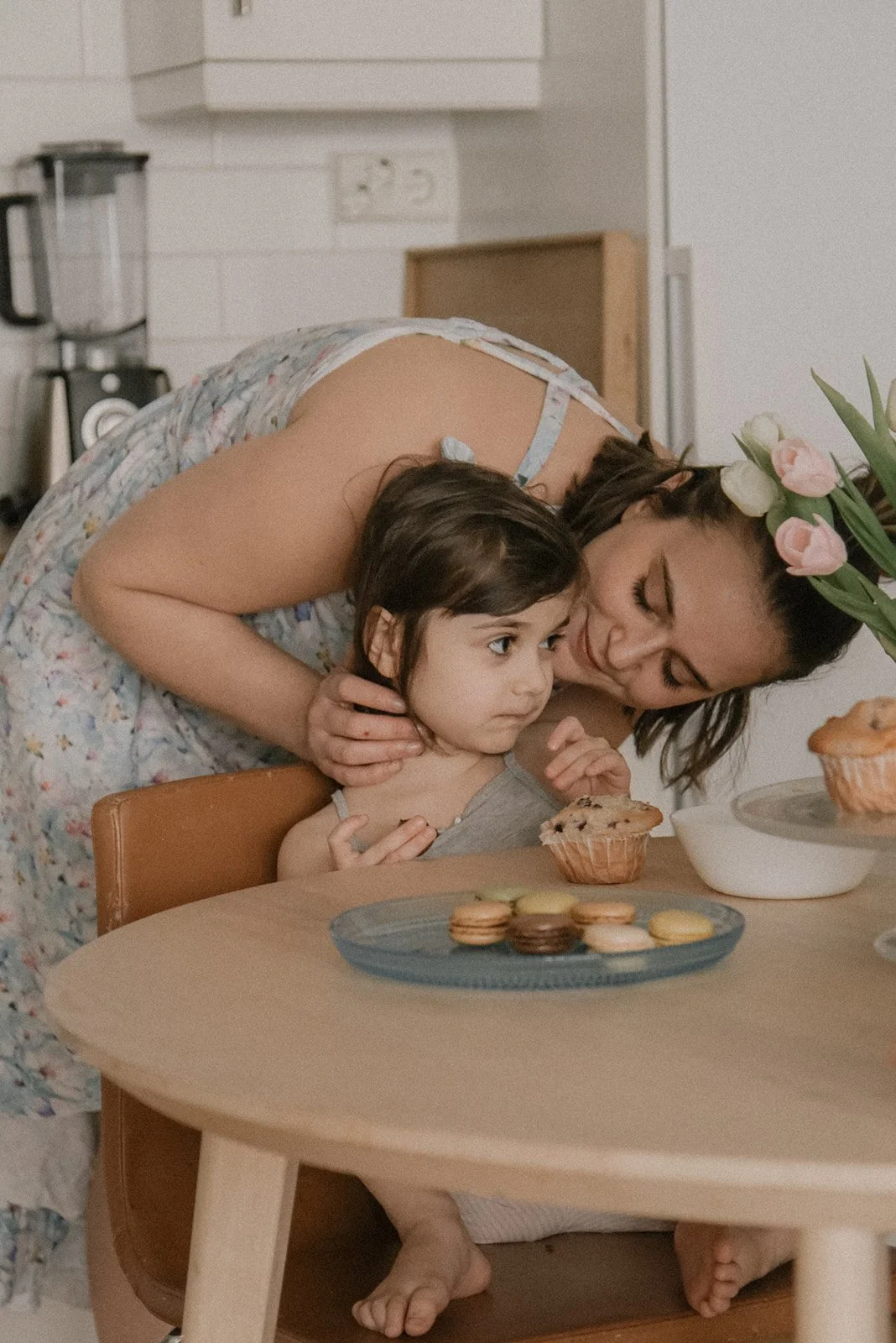 Lapsi istuu keittiön pöydä ääressä ja äiti antaa lämpimän halauksen. Perhekuvaus Espoo.