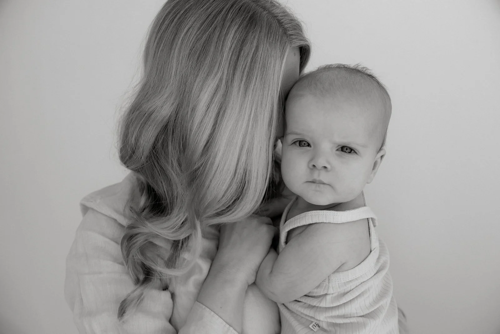 Äiti halaa vauvaa lempeästi. Äiti-lapsivalokuvaus valokuvausstudiolla.