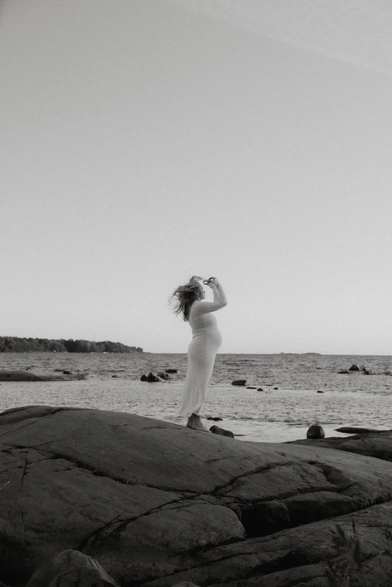 Mustavalkoinen valokuva raskaana olevasta äidistä rannalla. Kuvannut Heidi Väisänen.