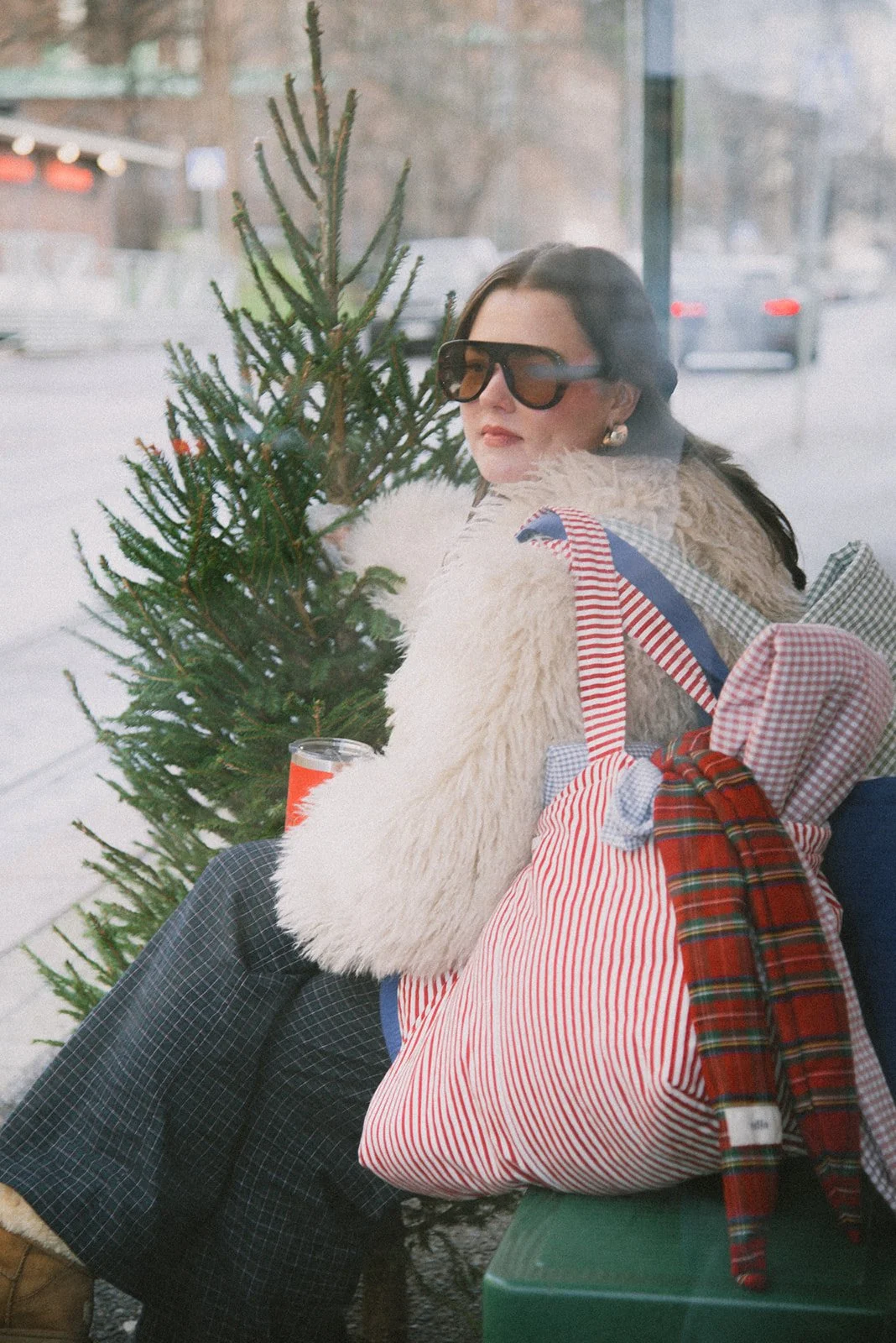Edlan brändikuvaus Helsingissä. Yrittäjä istuu ratikkapysäkillä brändin laukut olalla ja pitelee joulukuusta.
