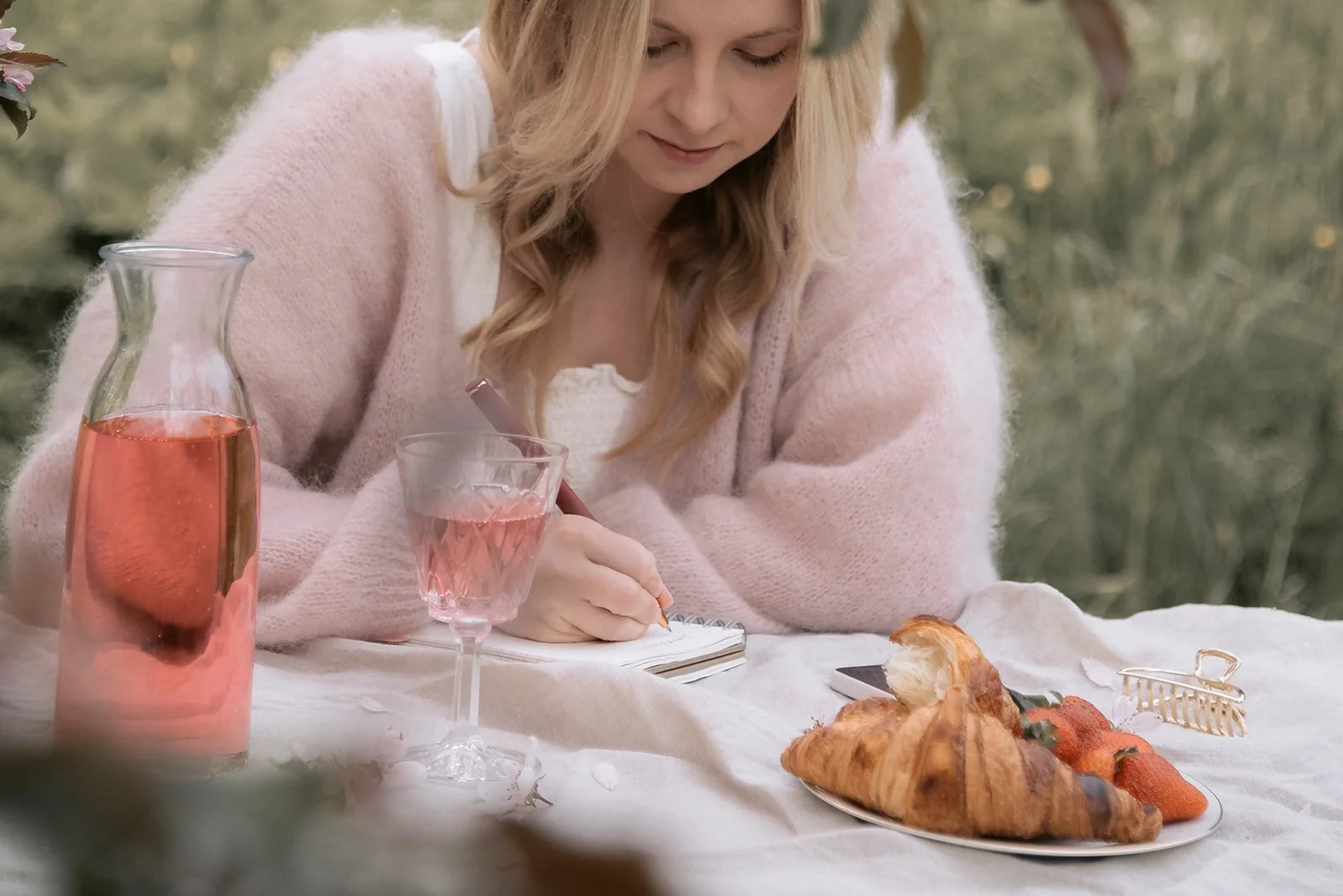 Yrityskuvaus luonnossa. Doula Jutta Alanen / Sunsynnytys istuu pöydän ääressä ja kirjoittaa muistikirjaan.