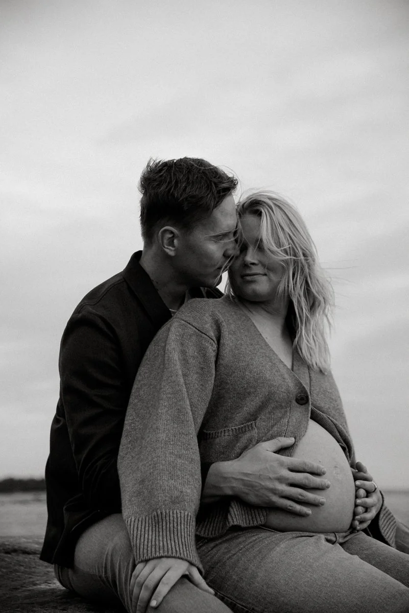 Pariskunta hellässä syleilyssä kalliolla. Odottava äiti on kääntynyt katsomaan miestä. Raskausajan kuvaus luontomaisemassa.