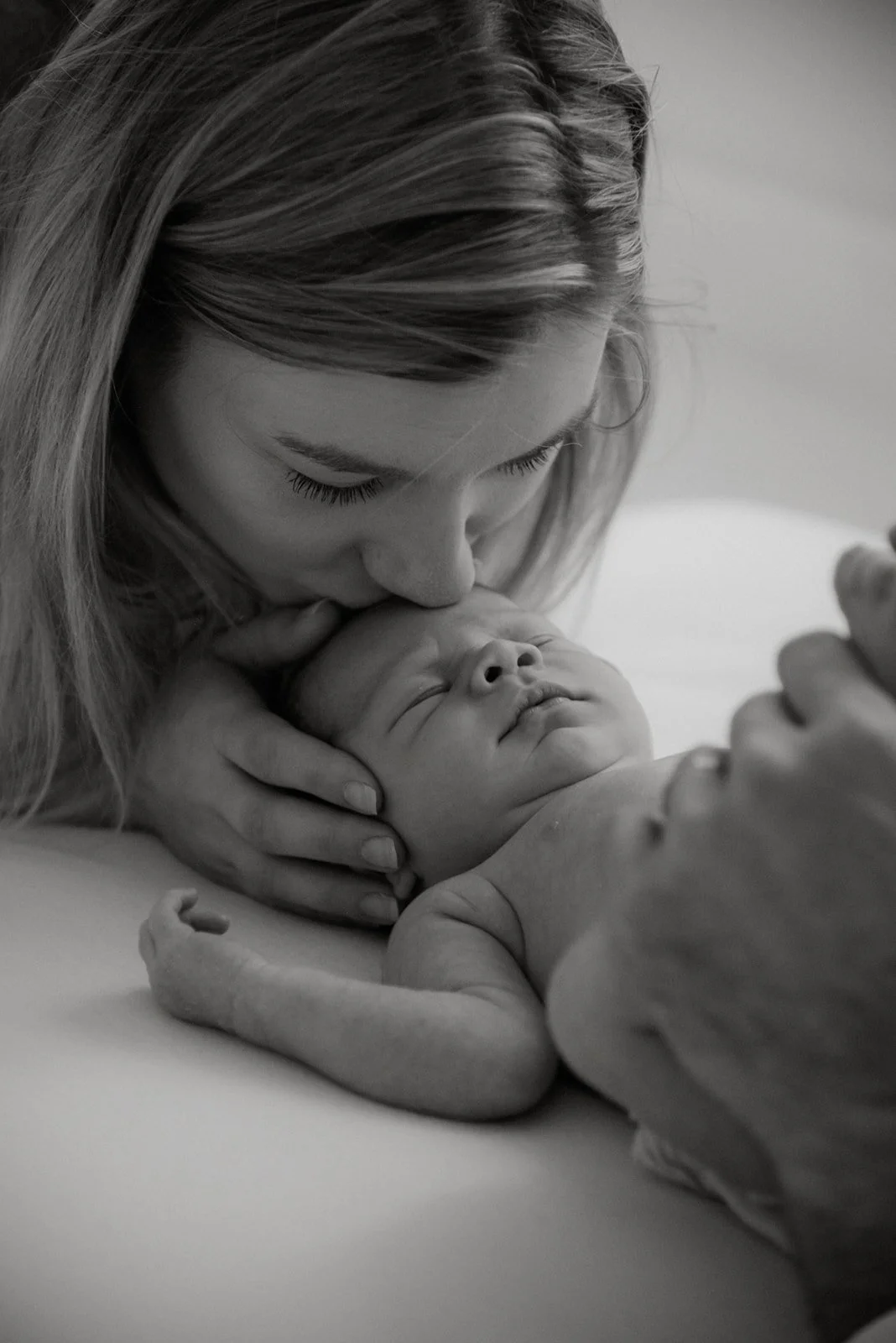 Vastasyntyneen kuvaus. Äiti suutelee hellästi vauvaa otsalle. Kuvan on ottanut vauvakuvaaja Heidi Väisänen.