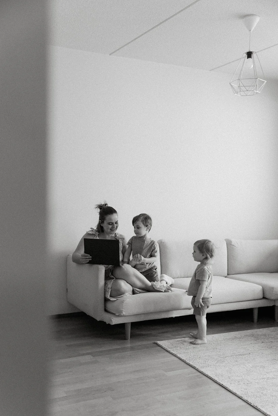 Perhekuva, äiti ja lapset yhdessä kotona mustavalkoisessa kuvassa.
