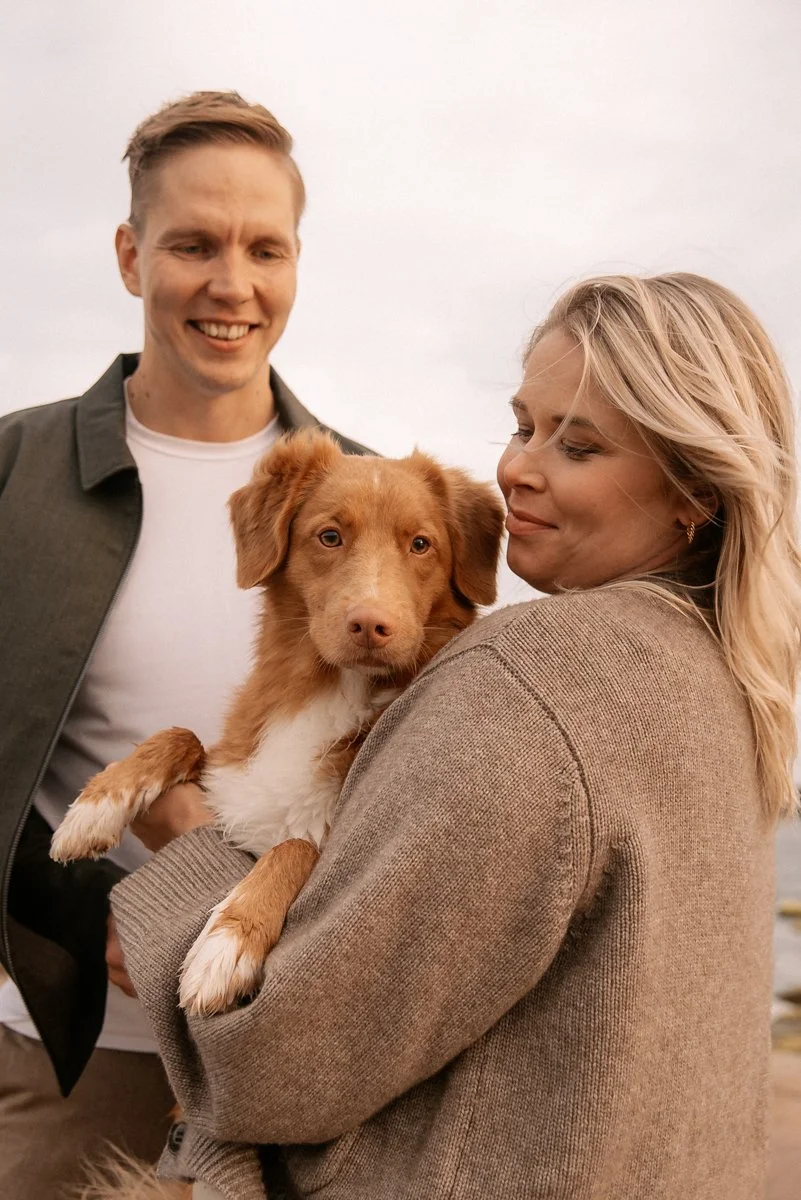 Odottava äiti pitelee perheen koiraa sylissään. Odotuskuvaus ulkona.