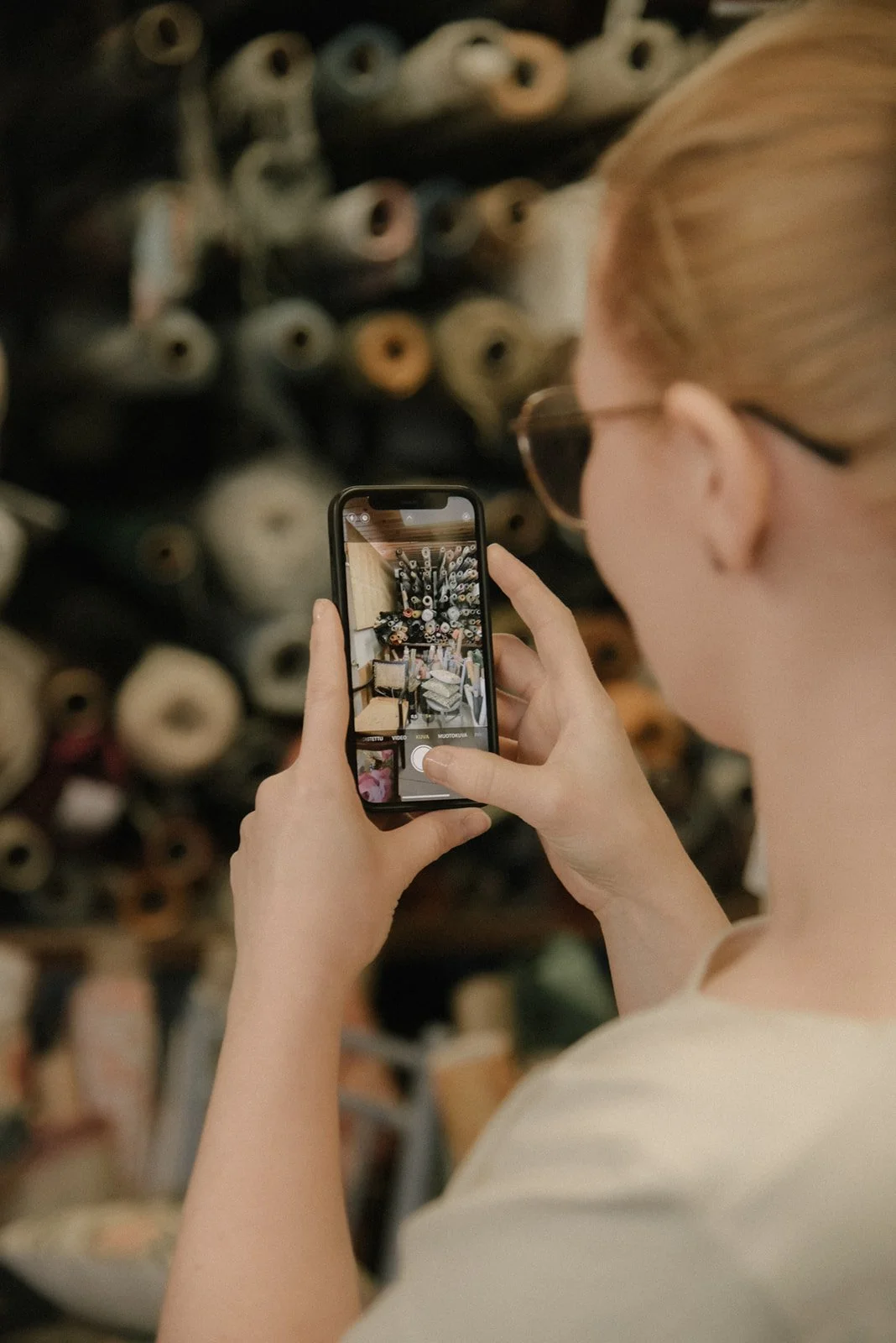 Verhoiluliike Eklundin brändikuvaus, yrittäjä ottaa kännykällä kuvaa kangasrullista.