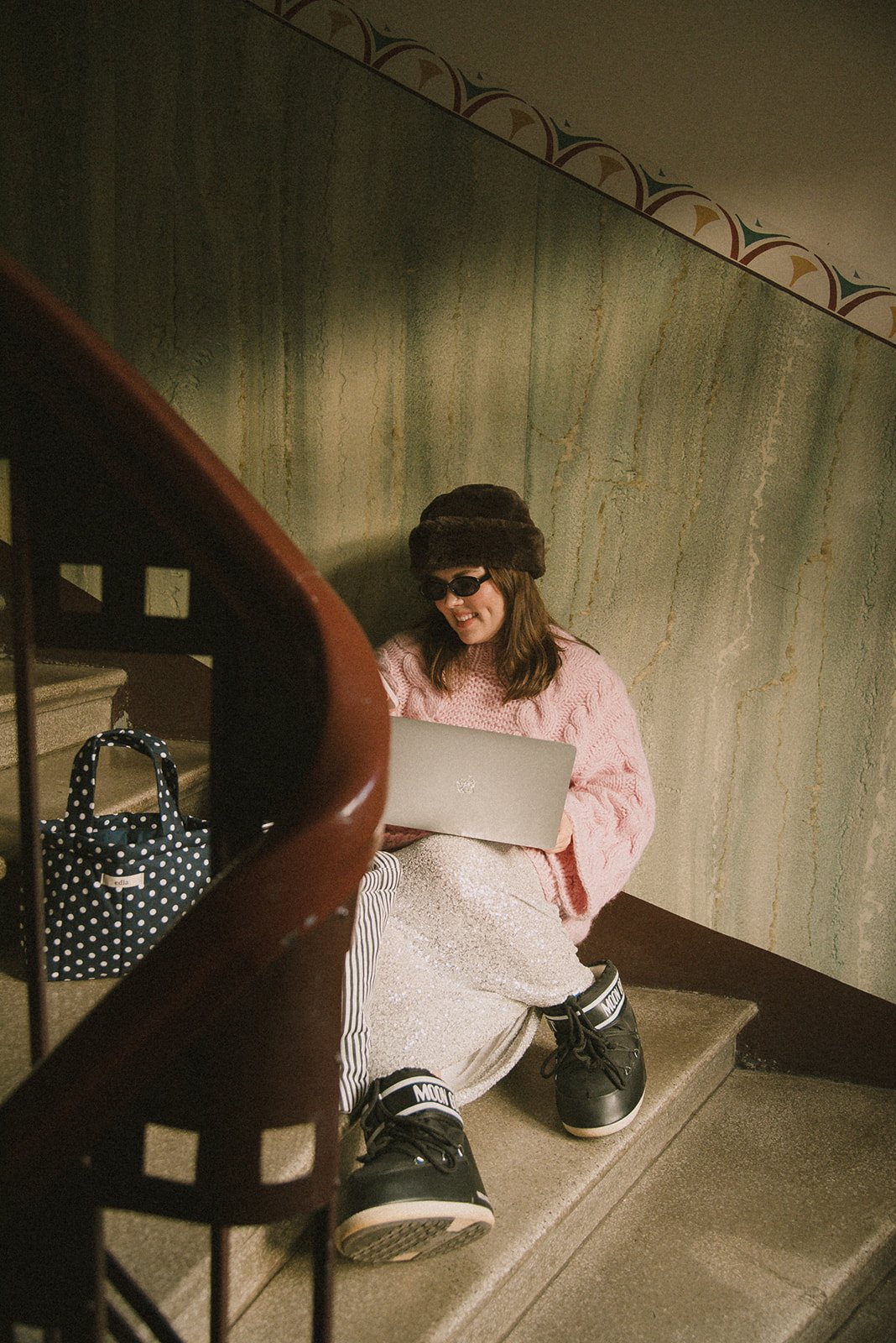 Edlan yrityskuvaus Helsingissä, yrittäjä istuu kauniissa portaikossa ja näpyttelee tietokonetta.