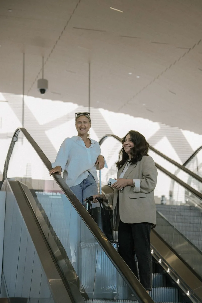 Neam Societyn brändikuvaus lentokentällä. Kaksi naisyrittäjää liukuportaissa.