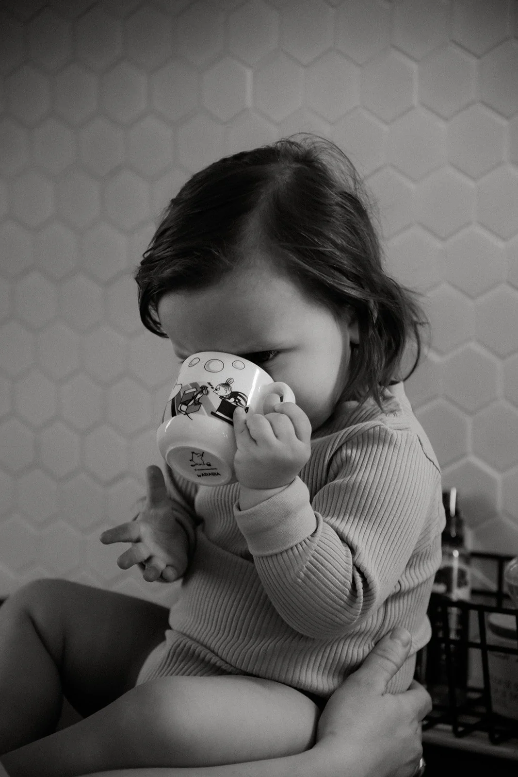 Mustavalkokuva, jossa pieni tyttö muki kädessään.