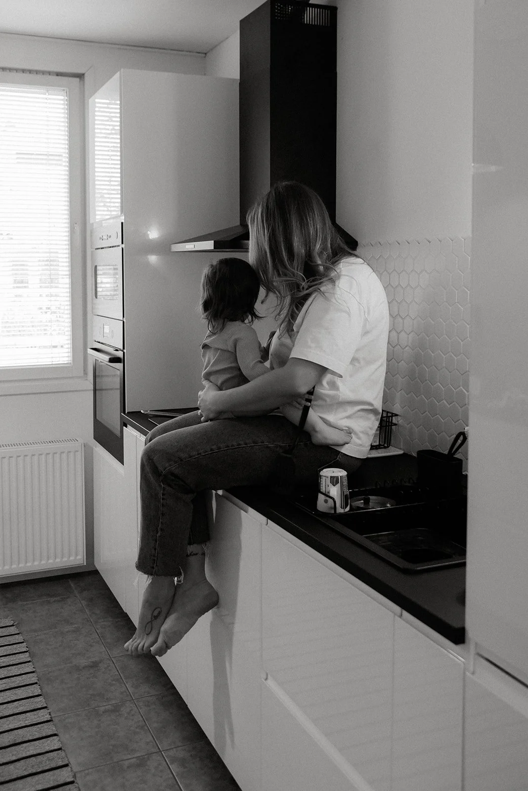 Äiti syleilee lastaan kotimiljöössä. Perhekuvaus kotona.