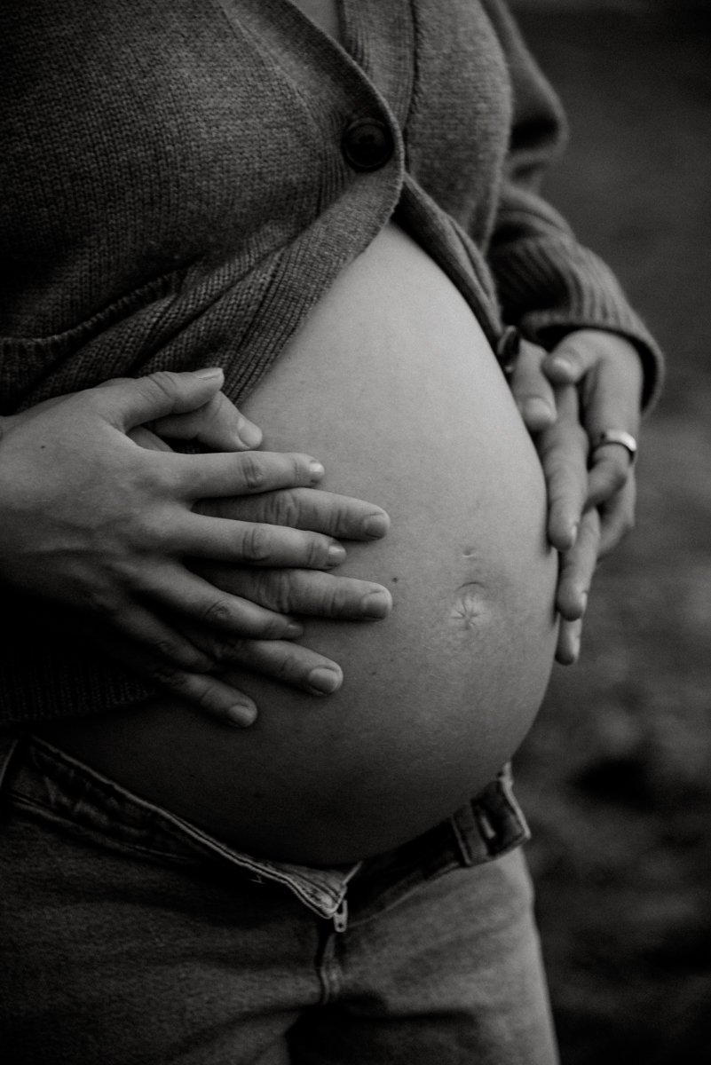 Vanhempien kädet raskausvatsan ympärillä. Odotusajan kuvaus Vantaa.