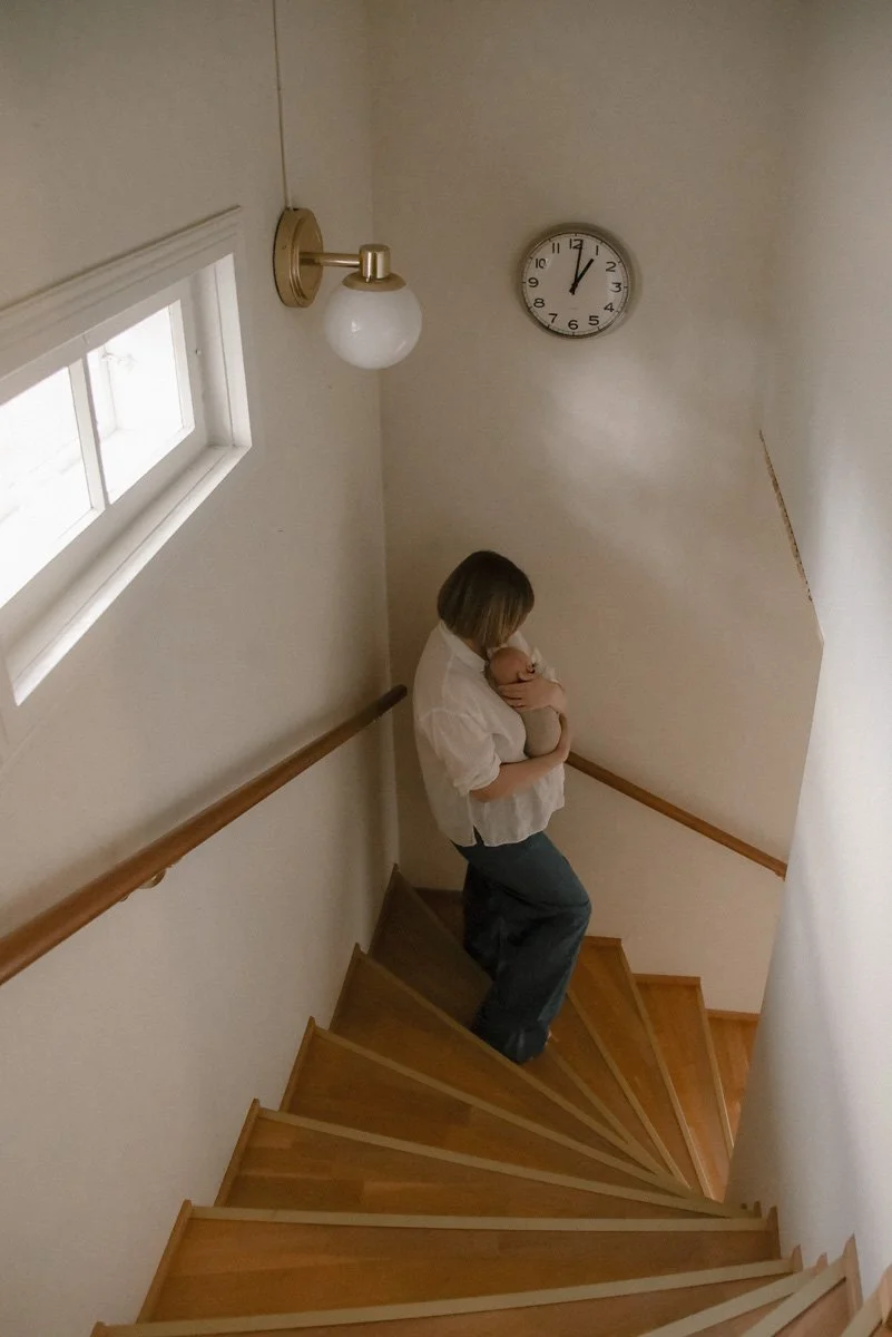 Äiti kävelee varovasti kodin portaita lapsen kanssa. Vauvakuvaus kotona.