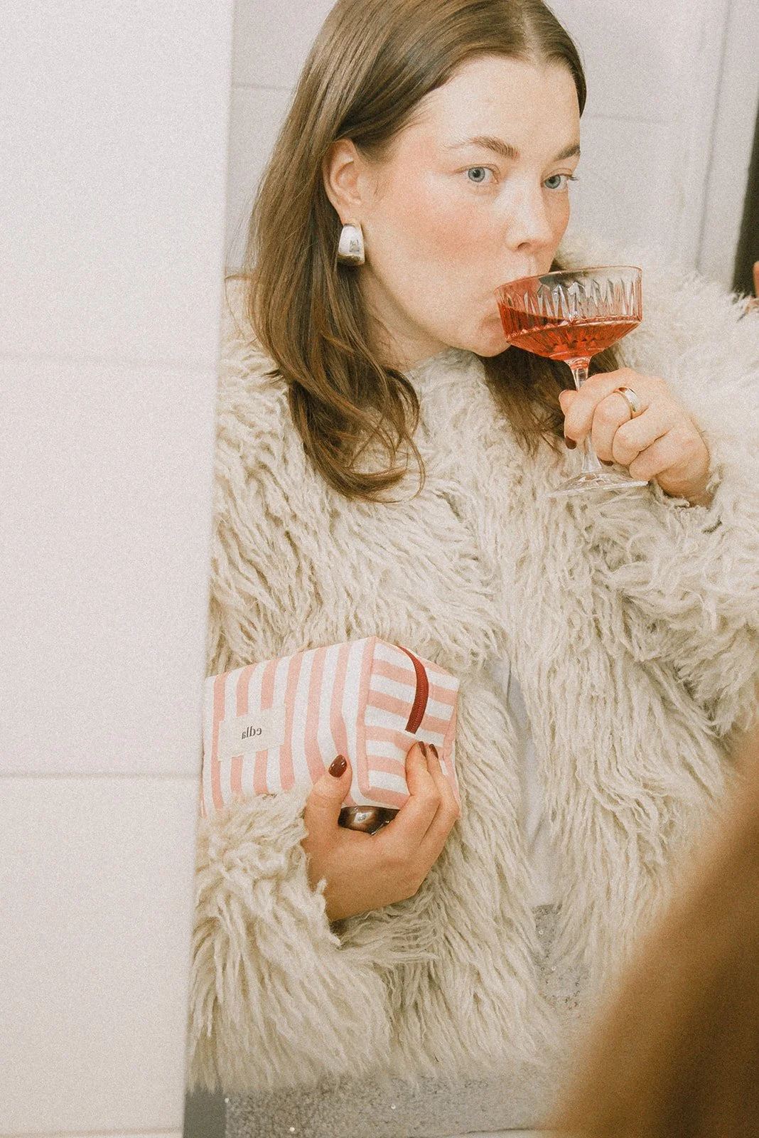 Edlan yrityskuvaus, yrittäjä siemailee drinkkiä brändin meikkipussi kainalossaan.