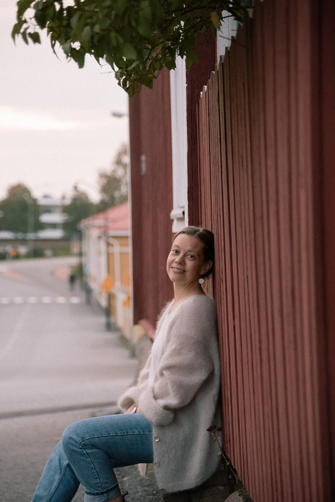 Yrityskuvaus ulkona. Yrittäjä katsoo suoraan kameraan ja nojaa talon puiseen ulkoseinään.