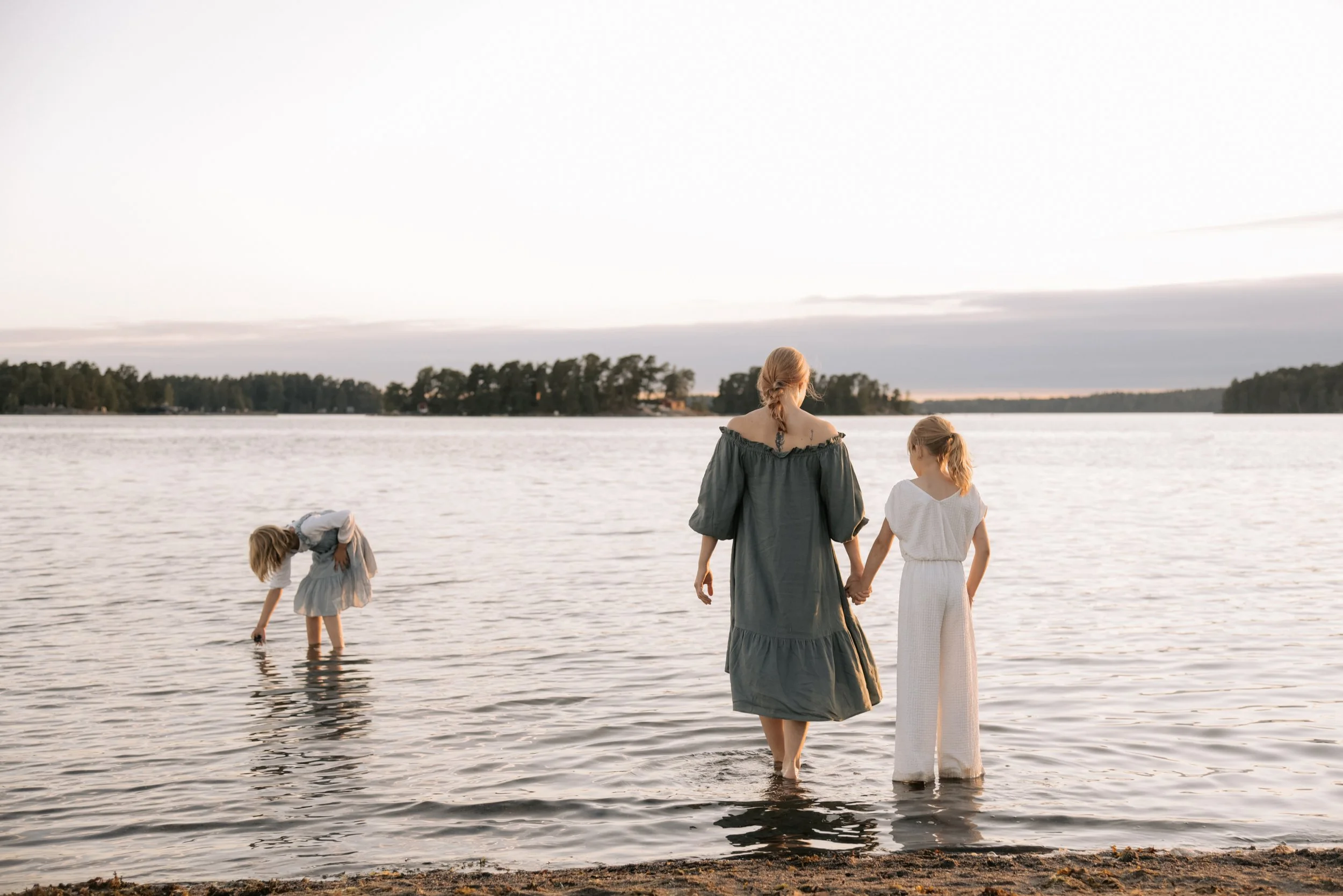 Perhekuvaus merimaisemassa, äiti ja kaksi lasta kahlaa vedessä. Kuvannut valokuvaaja Heidi Väisänen.