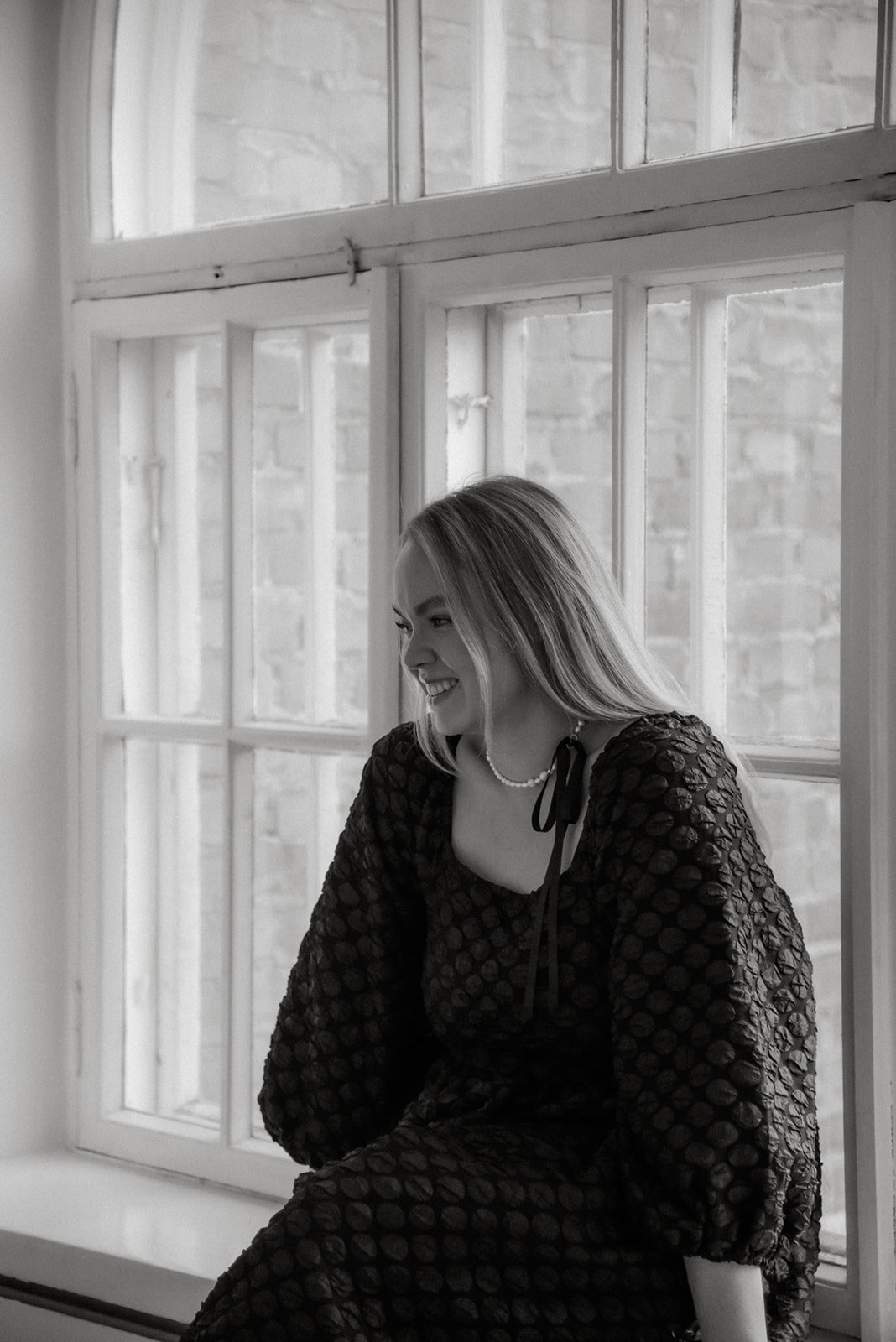 Brändikuvaus studiolla. Yrittäjä Jenni istuu ikkunalaudalla ja katsoo hymyillen kameraan.