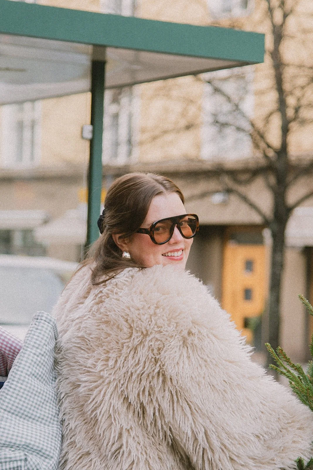 Edlan brändikuvaus, iloinen naisyrittäjä katsoo valoisassa kuvassa kameraan kaupunkimaisemassa.