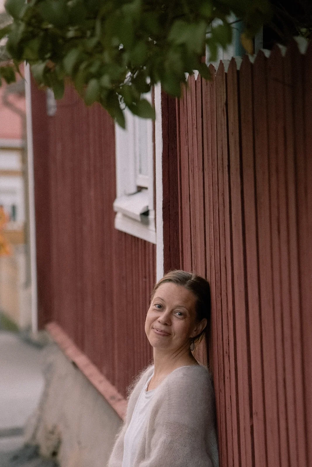 Brändikuvaus ulkona. Yrittäjä katsoo suoraan kameraan ja nojaa talon puiseen ulkoseinään.