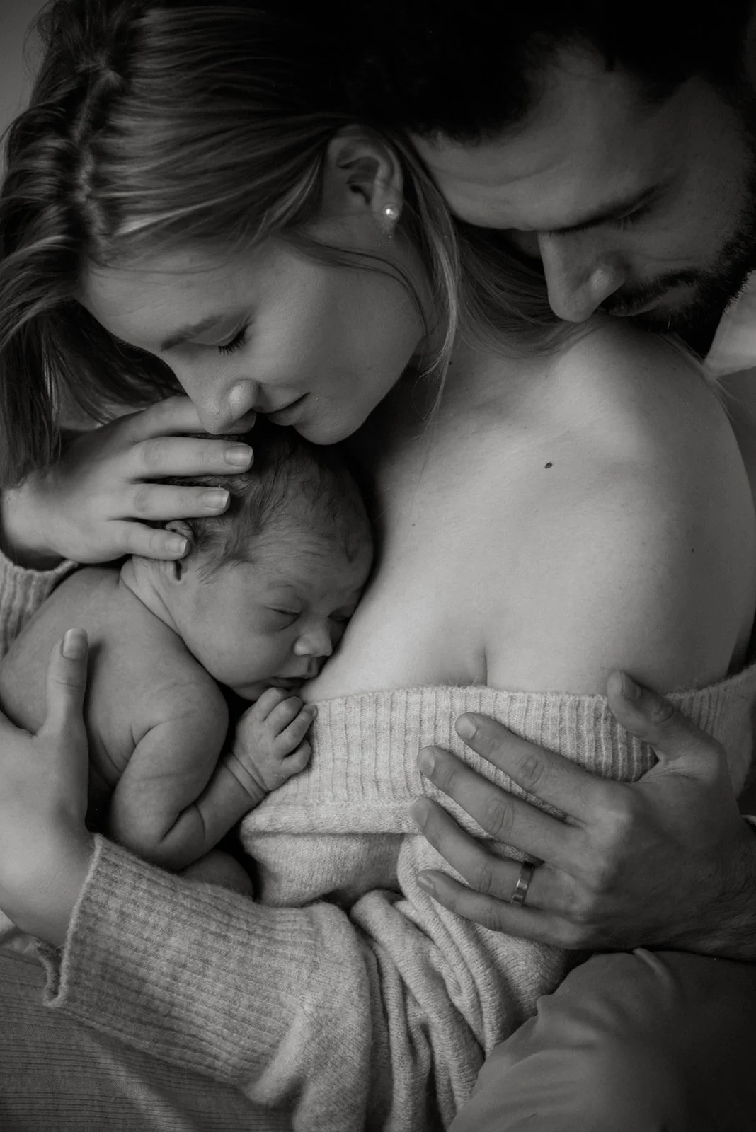 Mustavalkoinen kuva, jossa äiti ja isä halaavat pieni vastasyntynyt vauva sylissään. Kuvan on ottanut vauvakuvaaja Heidi Väisänen.