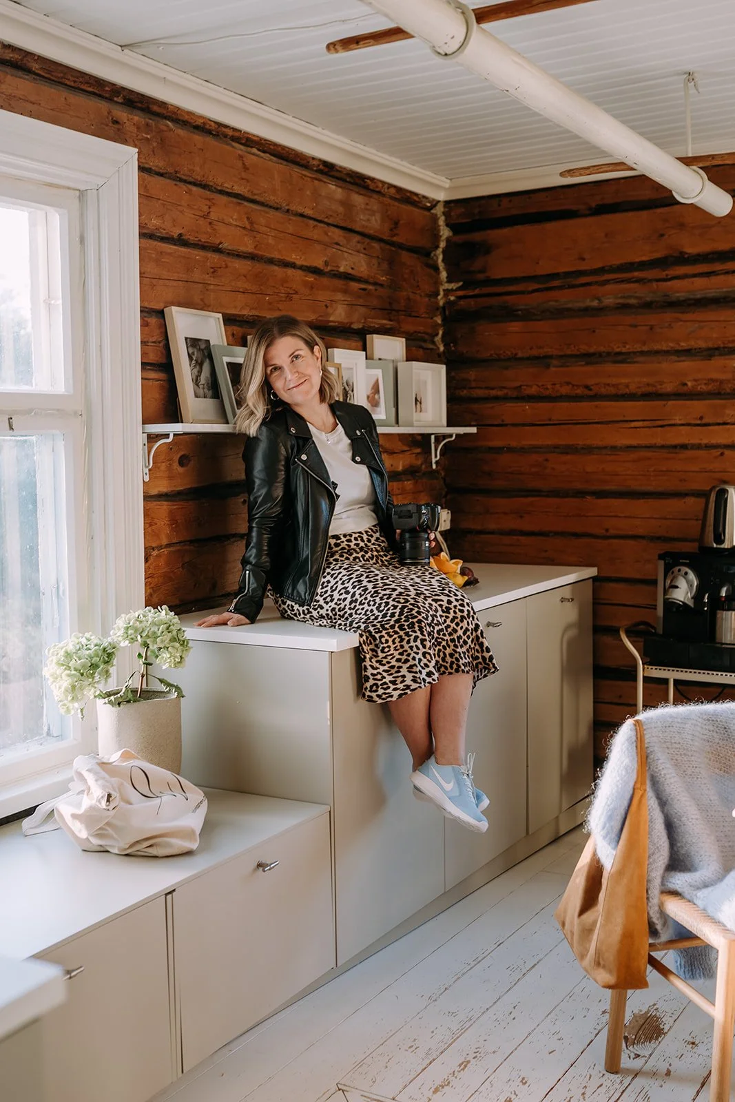 Valokuvaaja Heidi Väisänen istuu tason päällä, pitelee kameraa kädessään ja hymyilee