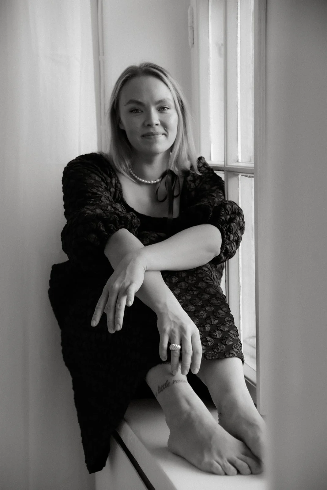 Yrittäjän brändikuvaus valoisassa studiossa. Jenni Boughanmi istuu ikkunalaudalla hymyillen.