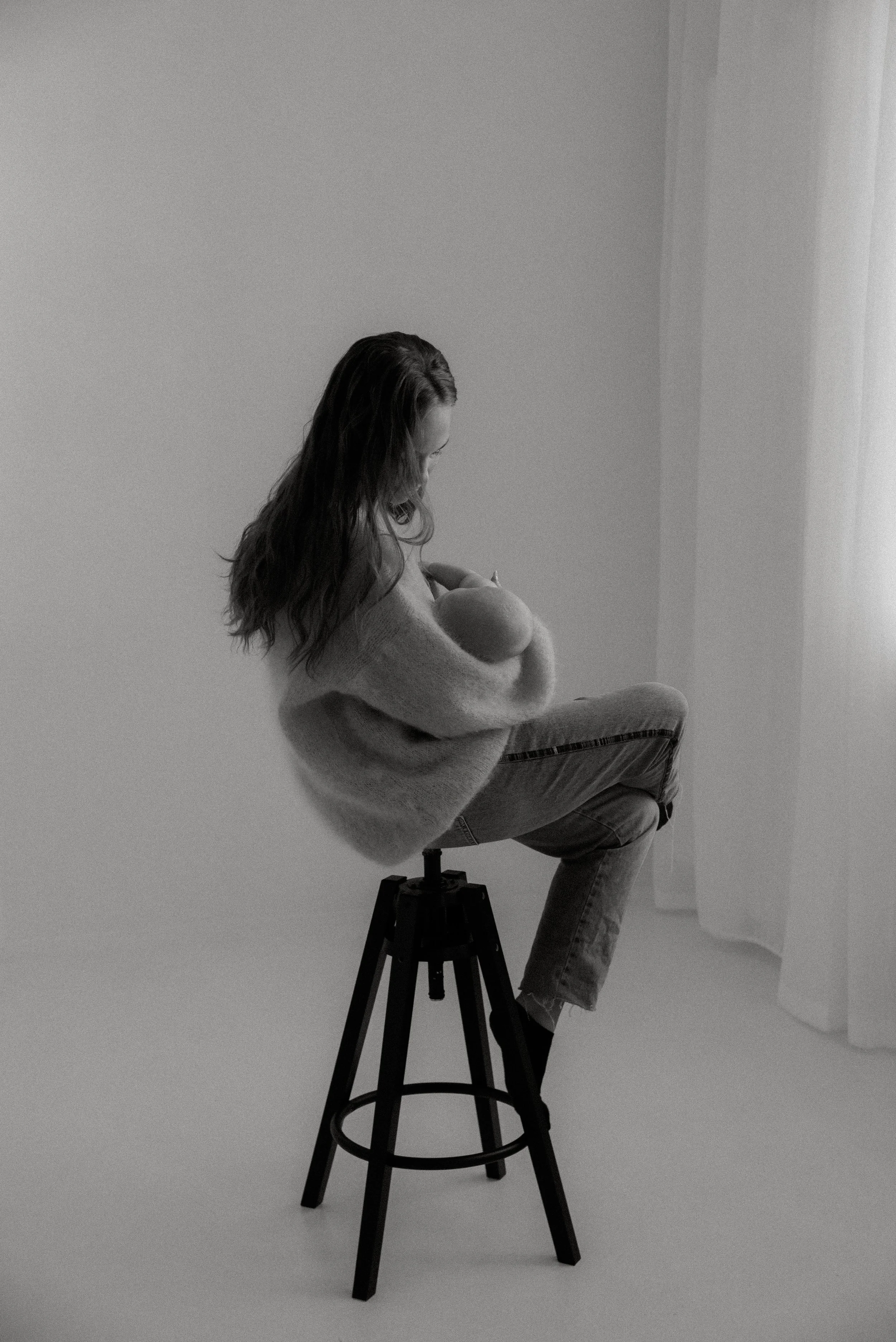 Äiti- ja lapsikuva, jossa äiti pitää lasta sylissä ja istuu korkealla tuolilla.