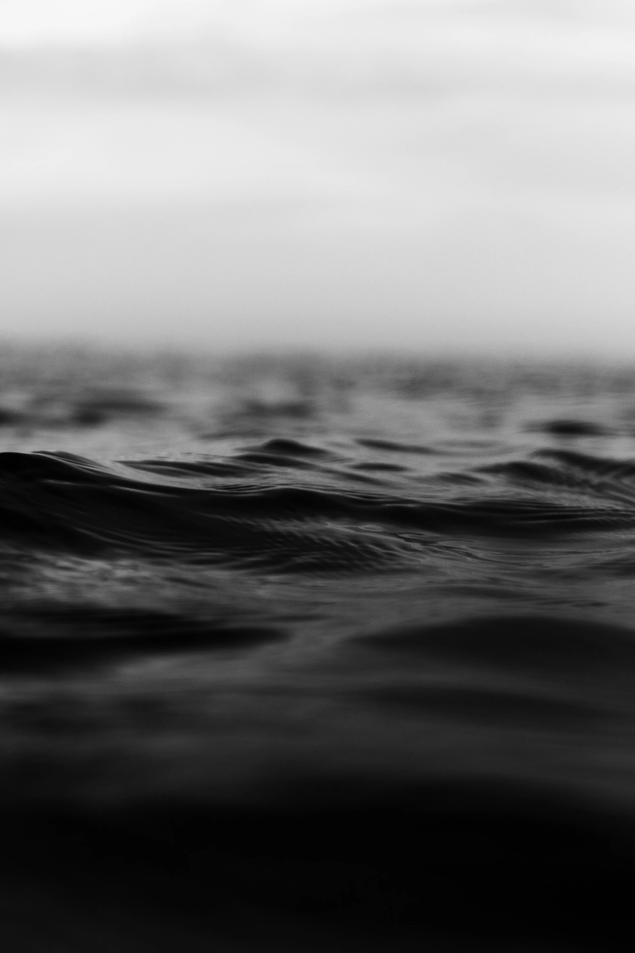 Black and white image of ocean waves with a soft sky background.
