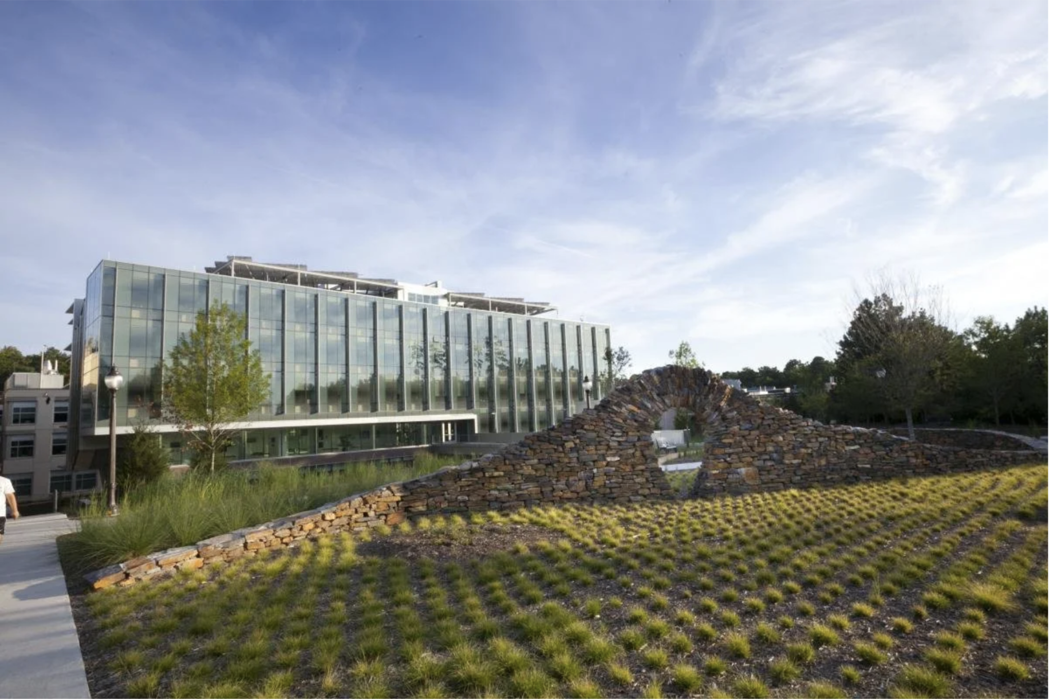 Modern glass building with a stone arch feature and landscaped greenery in the foreground