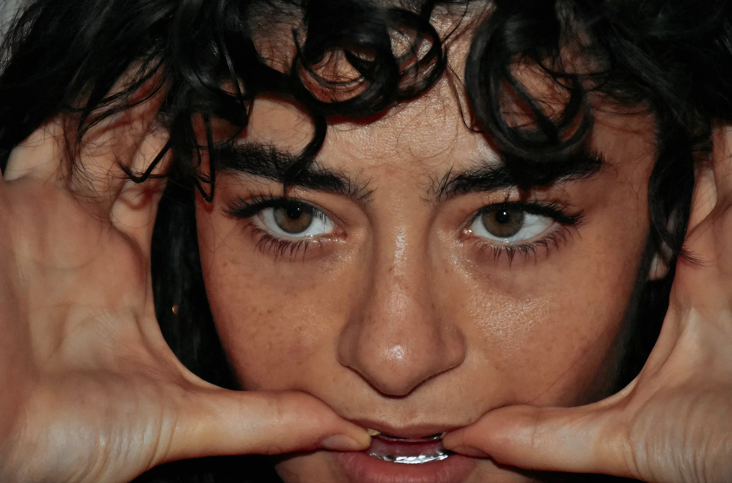 Primo piano di una donna con cappelli sulla testa e occhi azzurri che tocca il viso con entrambe le mani.