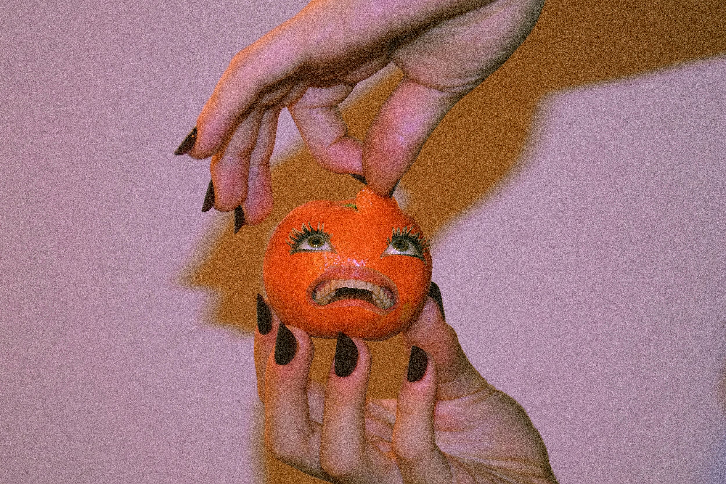 Una persona tiene in mano un mandarino con un volto disegnato e dettagli umani, come occhi e bocca, che esprime disgusto.