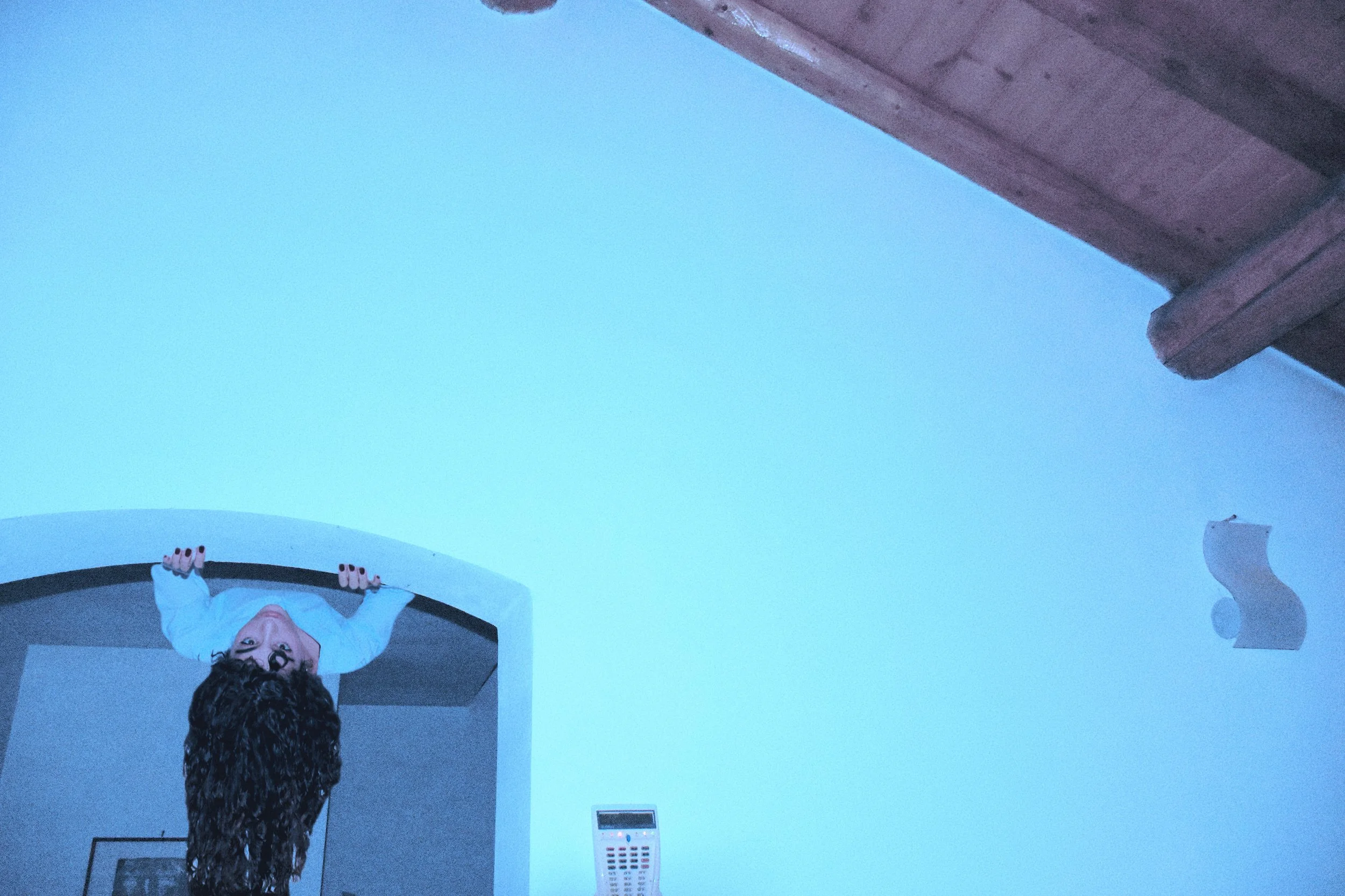 Persona che si appende con le mani alla cornice di una porta, con i piedi sospesi nel soffitto, in un ambiente domestico. L'immagine è scattata dall'angolazione inferiore, con un soffitto in legno visibile in alto a destra.