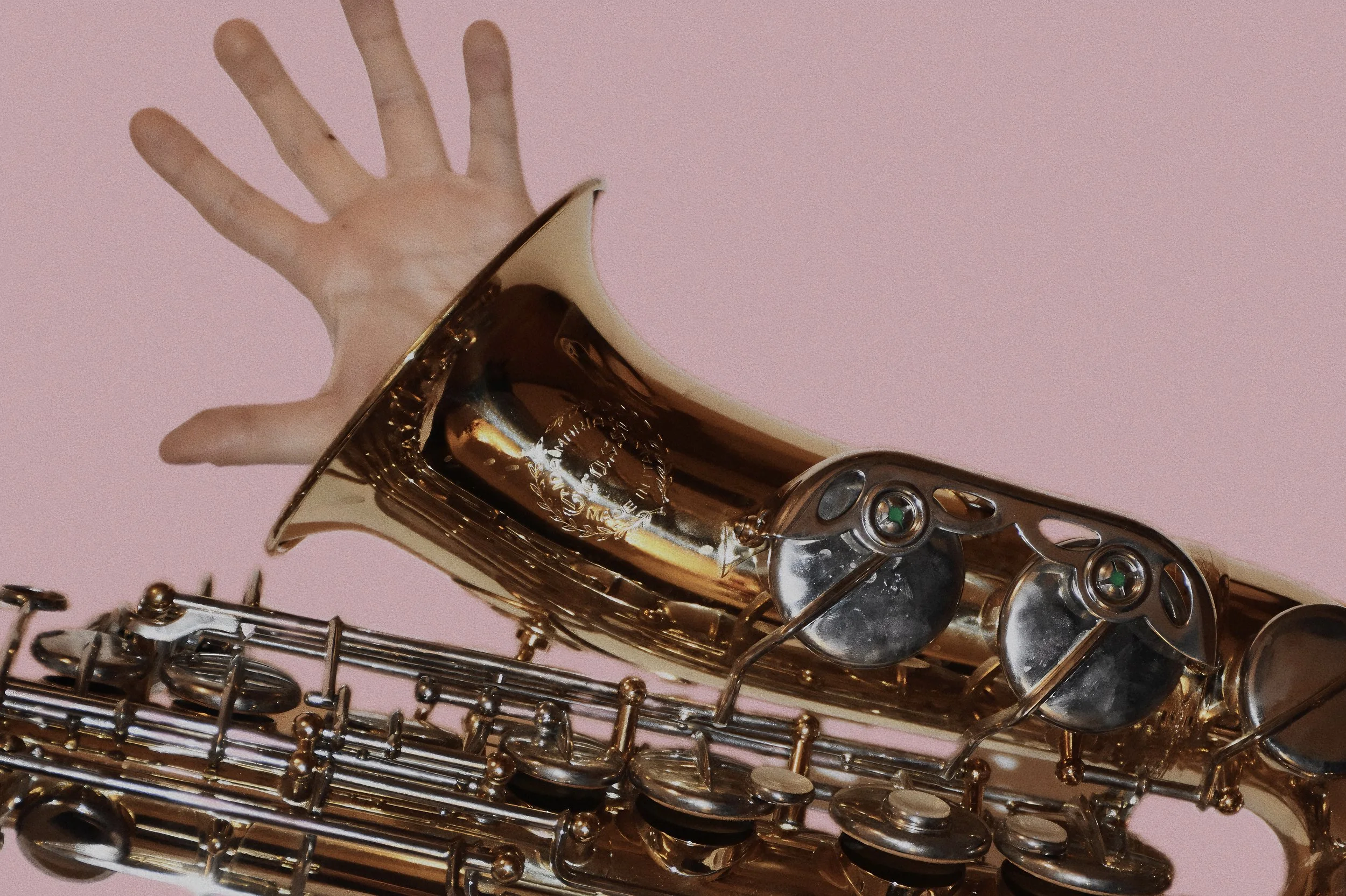Sax tenore dorato con una mano sopra contro uno sfondo rosa.
