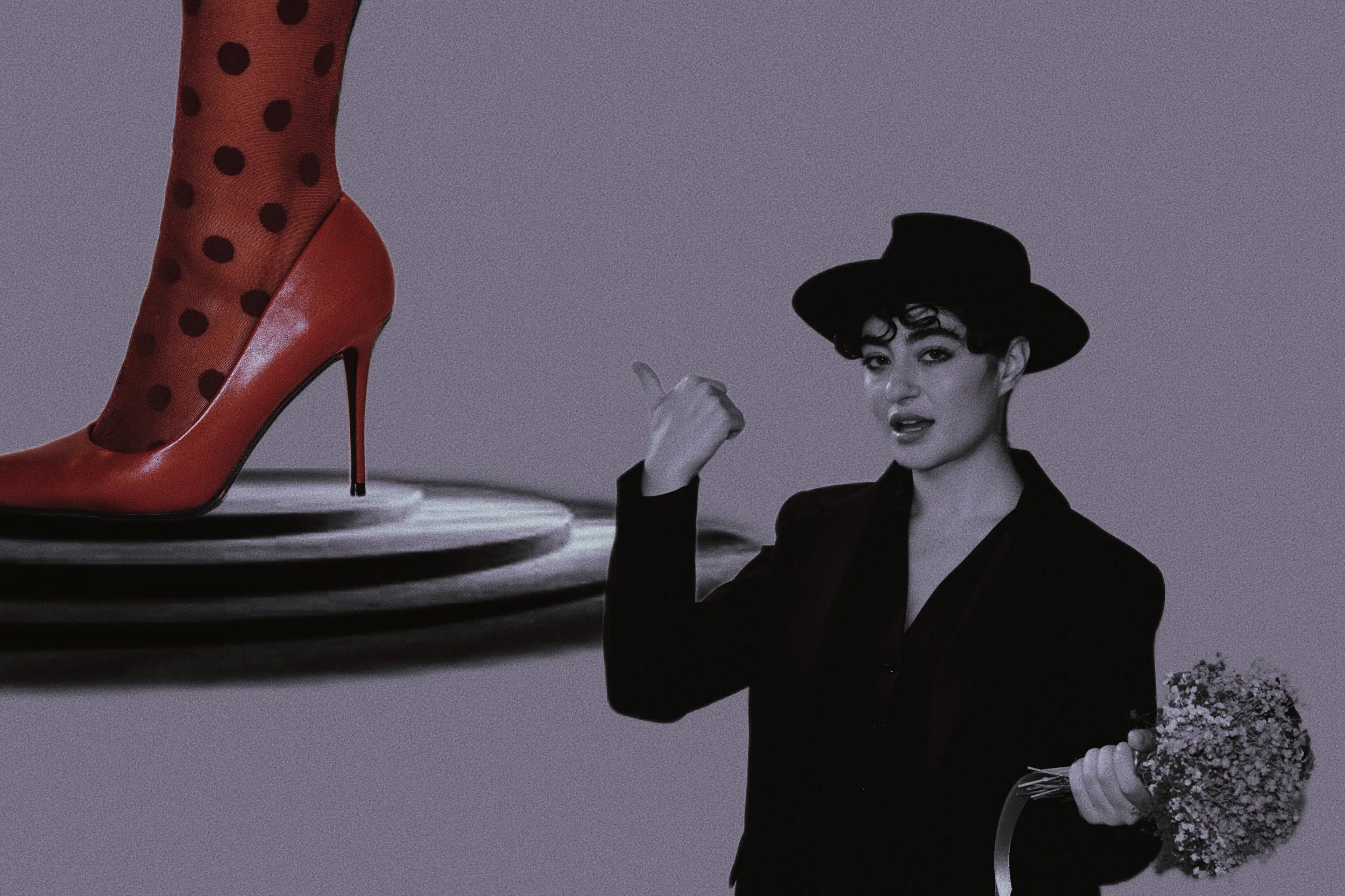 Immagine in bianco e nero di una donna con cappello nero che tiene un mazzo di fiori, mostra il dito medio e guarda verso la fotocamera. Sul lato sinistro, c'è un primo piano di una scarpa rossa con calzino a pois.