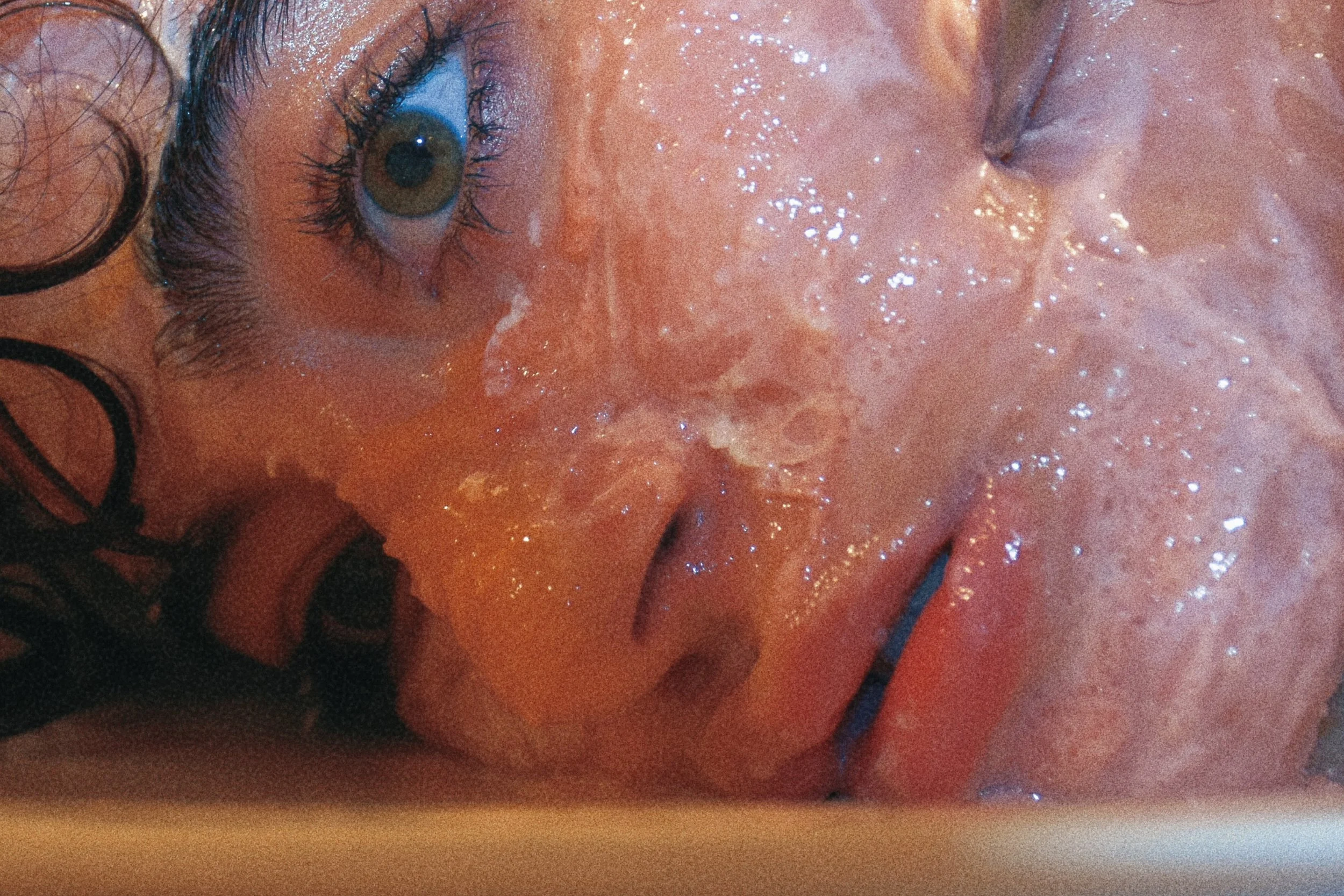 Primo piano di un volto umano bagnato con un occhio visibile, pelle lucida e capelli ricci.