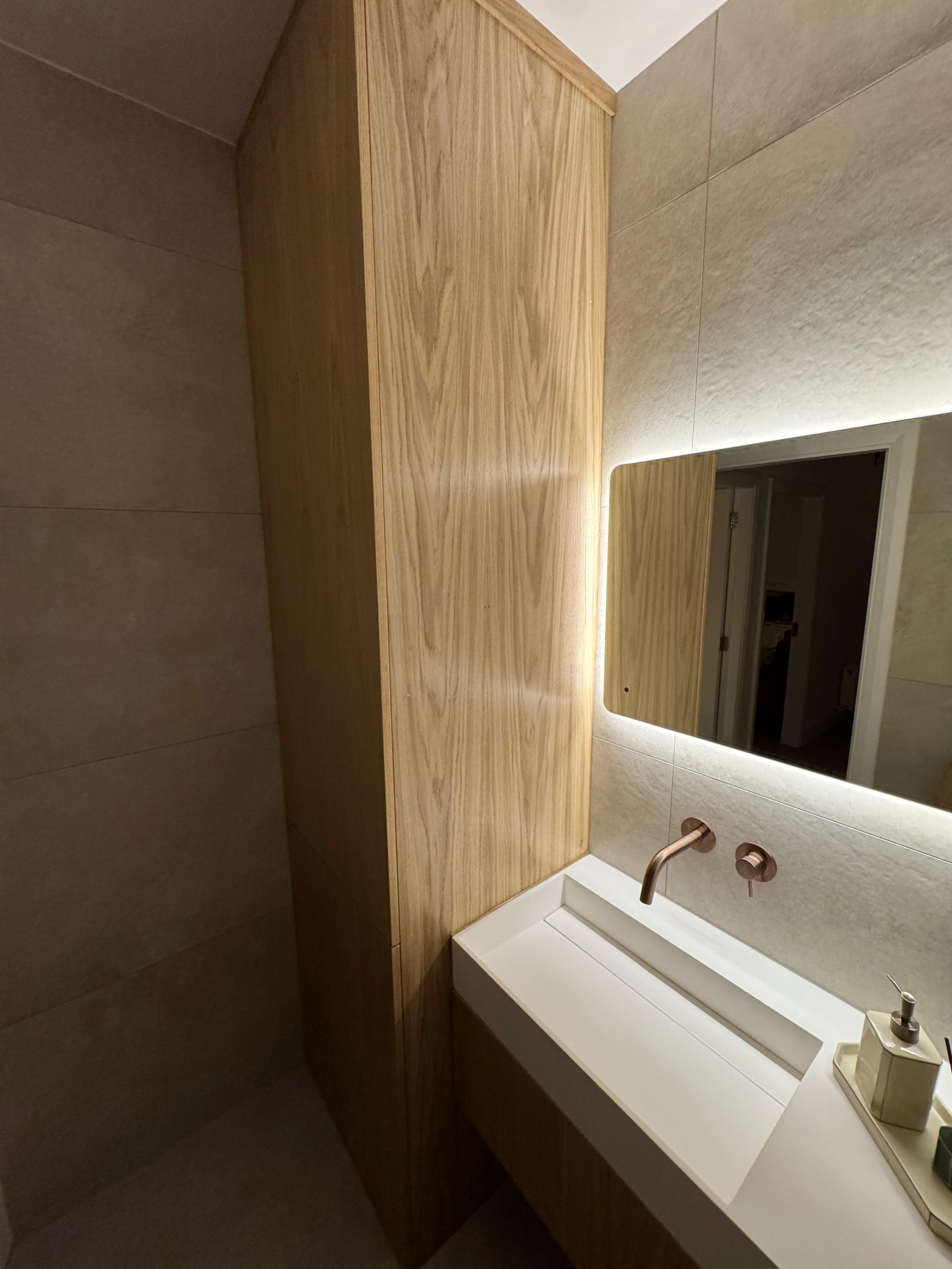 Modern bathroom with a wood cabinet next to a white sink and a large mirror with backlighting.