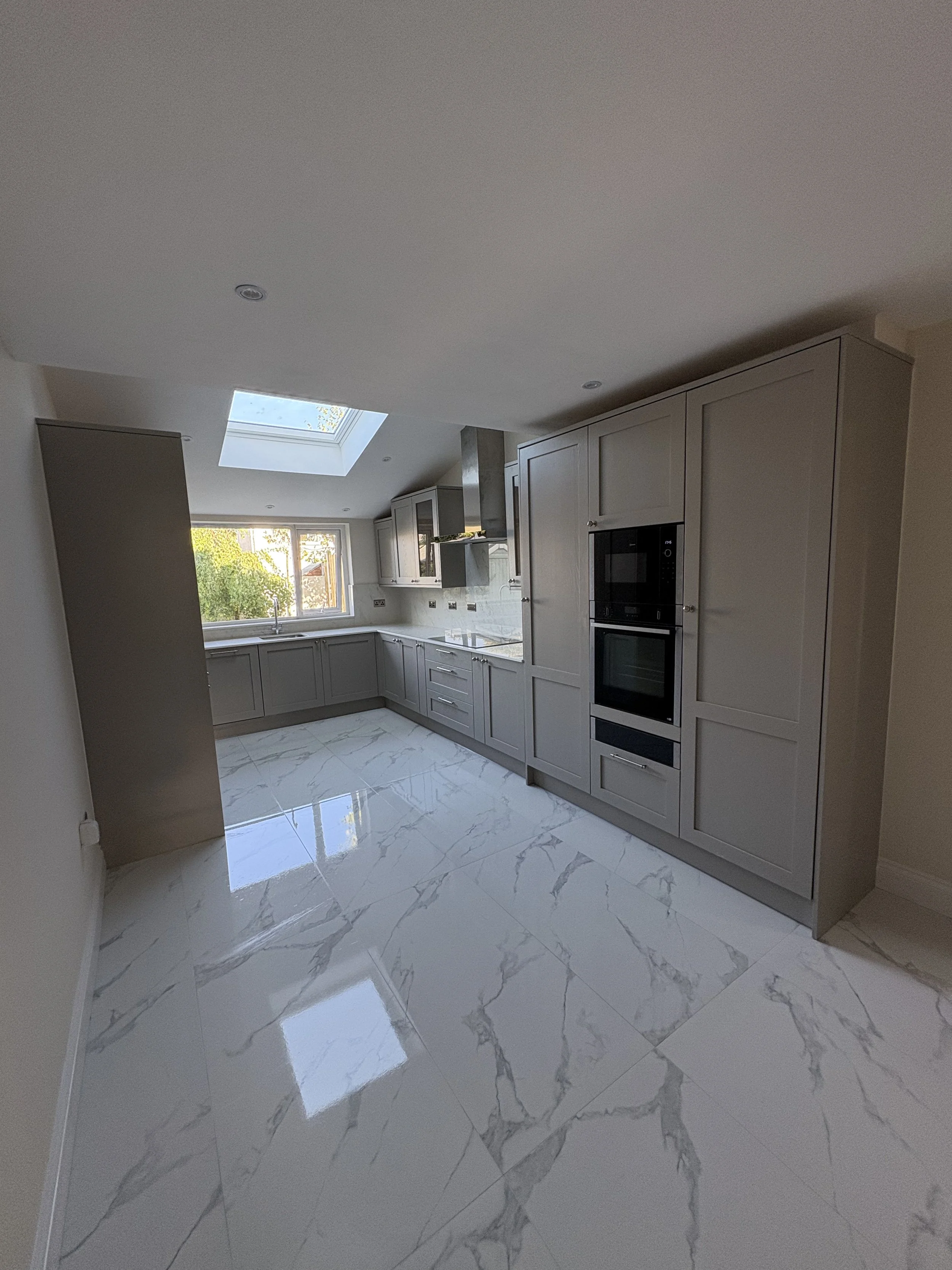Modern kitchen with gray cabinets, white marble floor, and large window with skylight.
