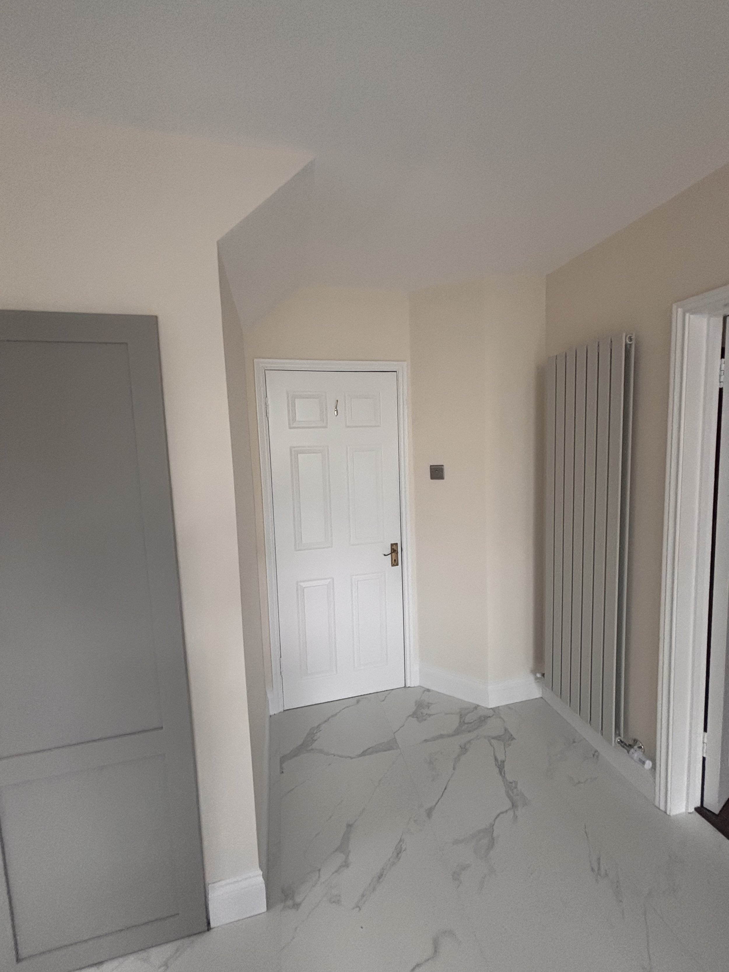 Interior corner of a room with white door, gray radiator, marble tile flooring, and light-colored walls.