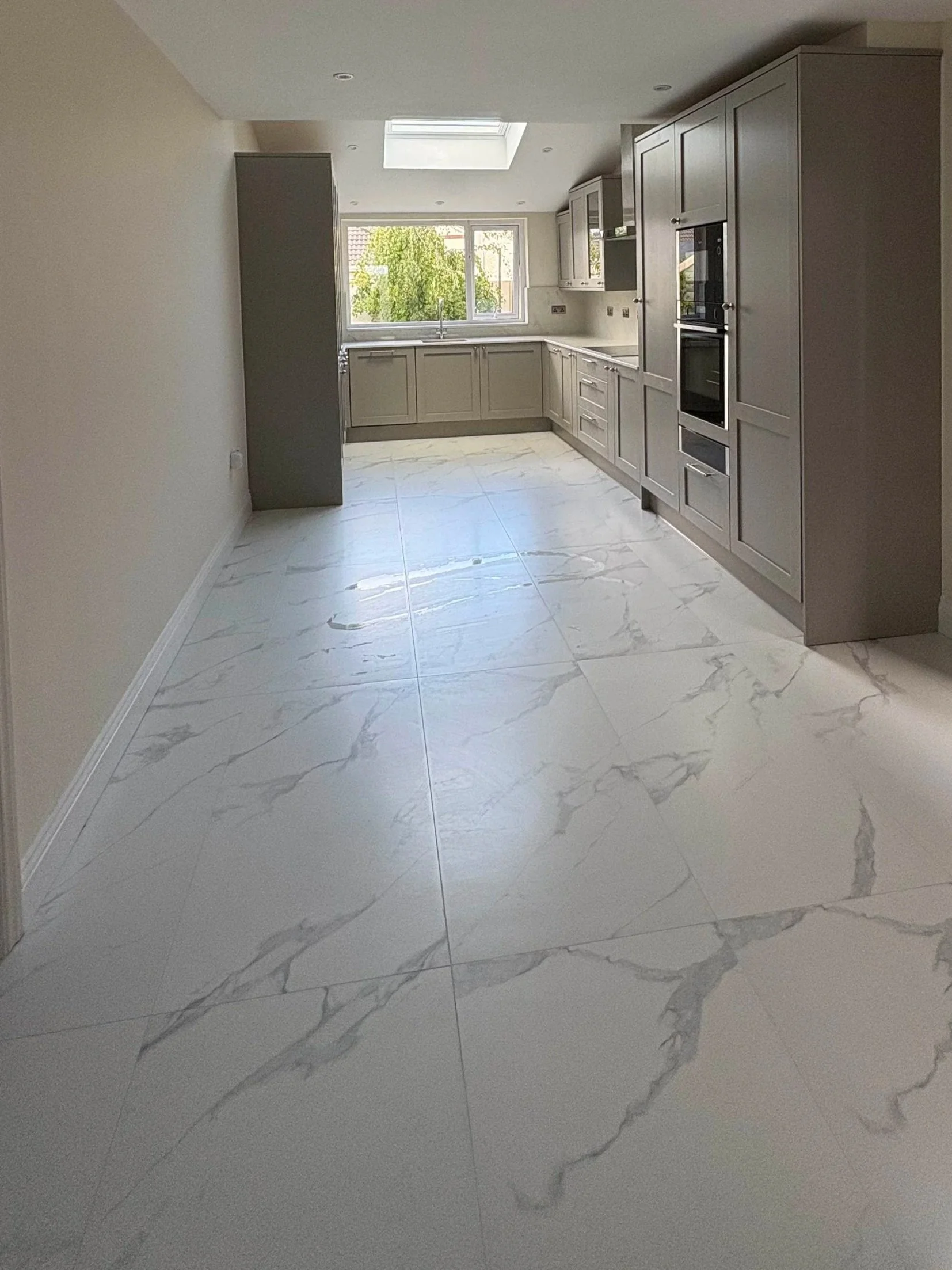 Room with a large skylight window in the ceiling and glass double doors leading outside to a patio and garden, with a wooden floor and white walls.