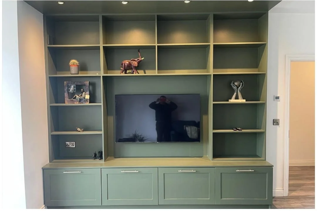 A large green entertainment center with open shelves, a central space for a flat-screen TV, and cabinets below. Decor includes a small potted cactus, a zebra figurine, a framed photo, and other small decorative items.
