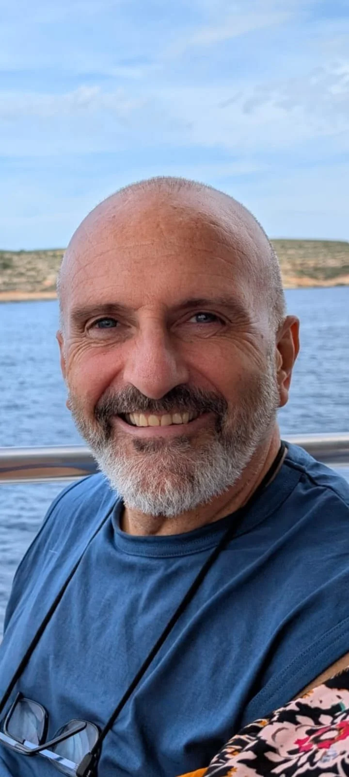 Close-up of smiling middle-aged man with a beard, on a boat with water and land in the background.