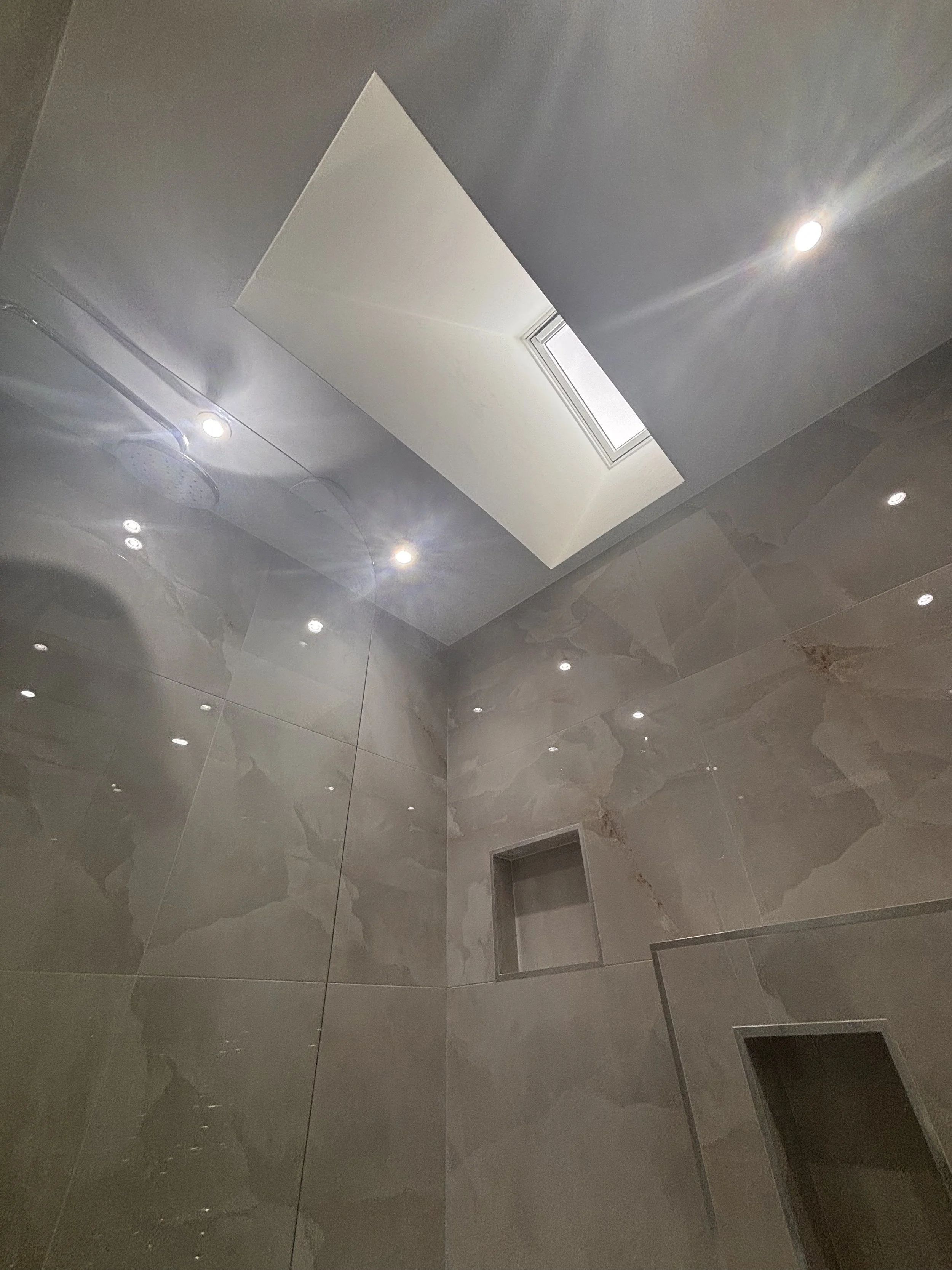 Interior shower with beige marble tiles, built-in shelves, and a skylight in the ceiling.