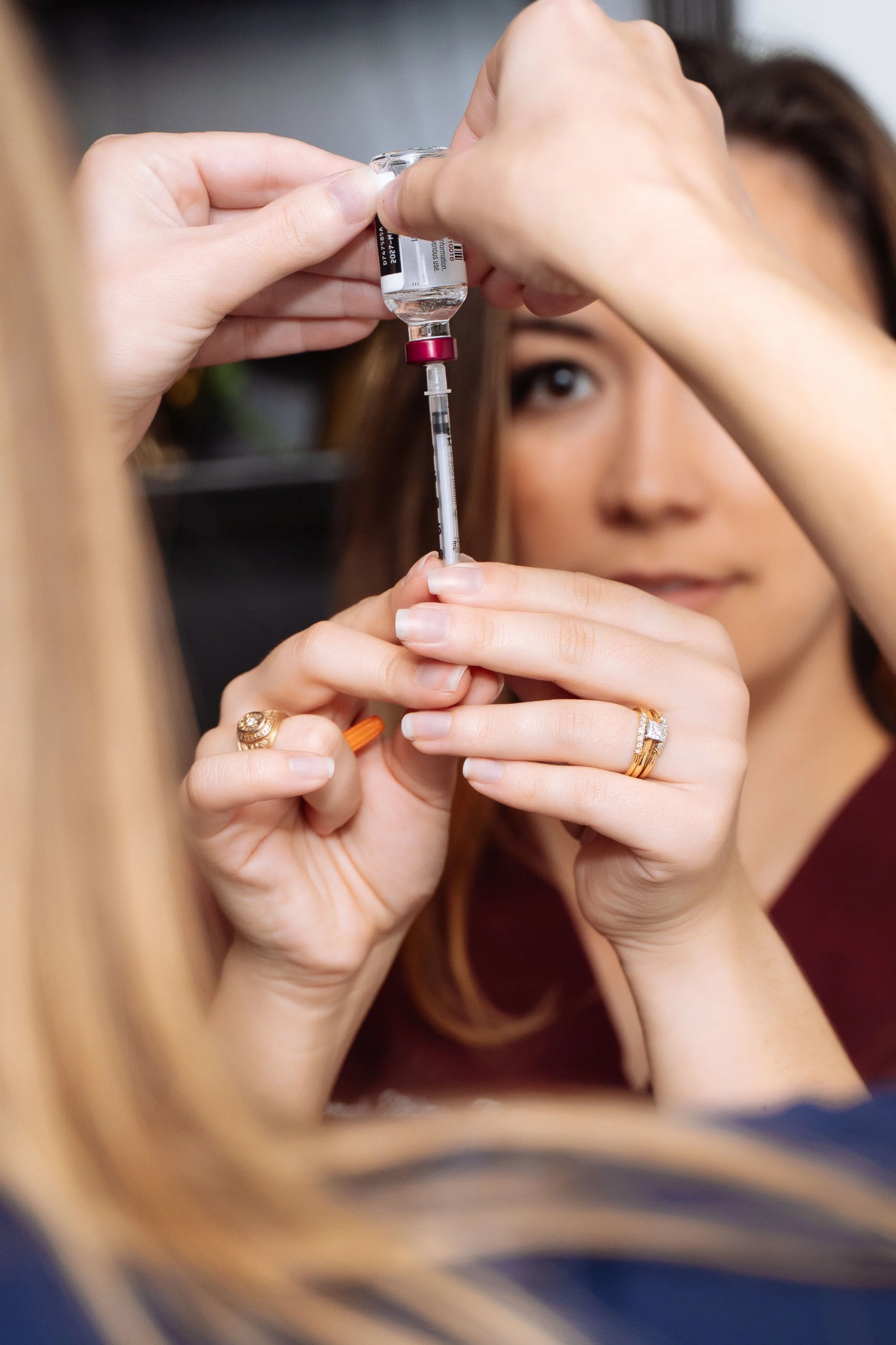 A healthcare professional prepares a syringe with a vaccine or medication, while a woman looks on closely.