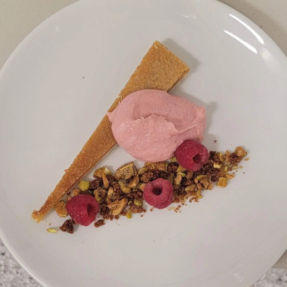 Slice of pie, raspberry sorbet, raspberries, granola, and nuts on a white plate.