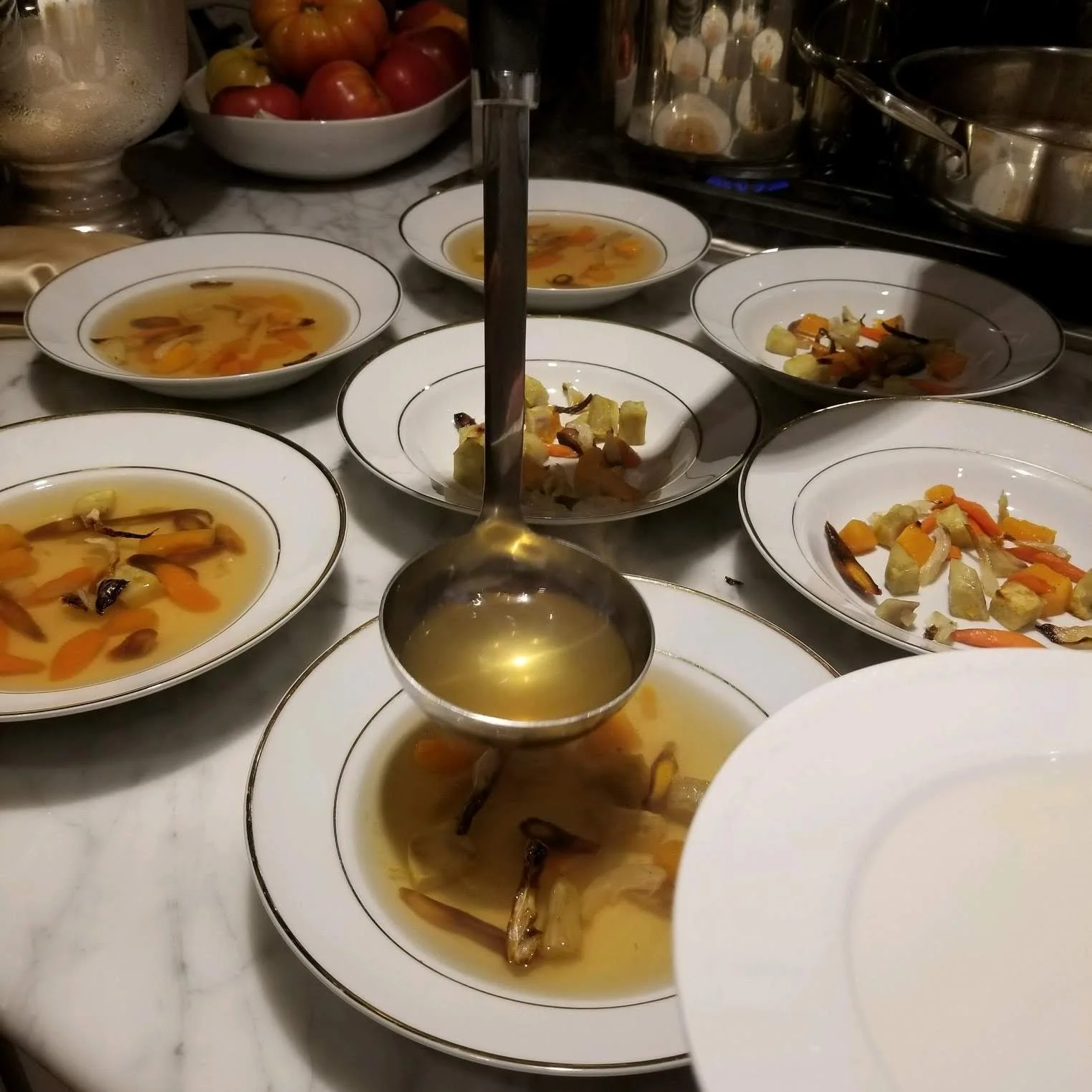 Several white porcelain bowls filled with vegetable soup and scattered roasted vegetables on a marble countertop.