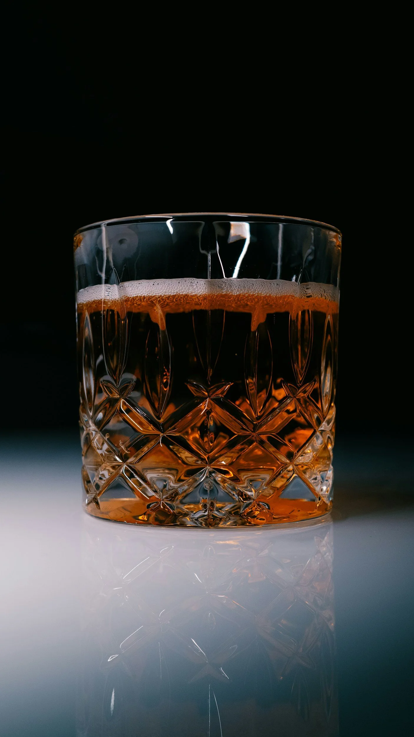 Close-up of a glass of whiskey with an intricate cut pattern on the glass, filled with amber-colored whiskey, against a dark background.