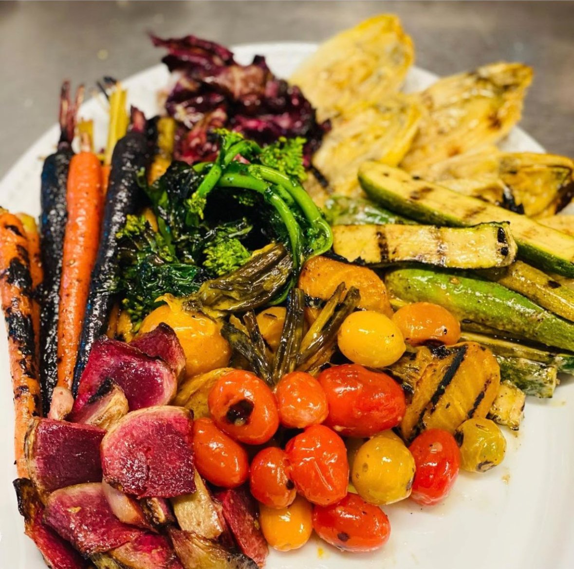 Assorted grilled vegetables including carrots, zucchini, cherry tomatoes, broccoli, beets, and eggplant on a white plate.