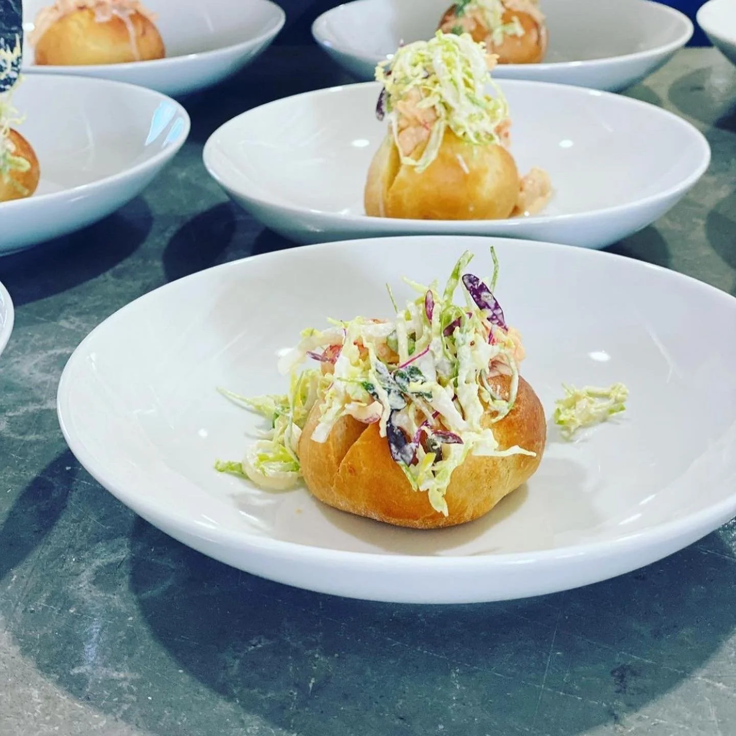 Mini baked potatoes topped with coleslaw served on white plates.